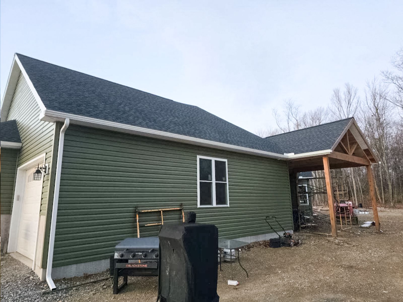 Green house exterior with white trim, small porch, and a black grill in the yard