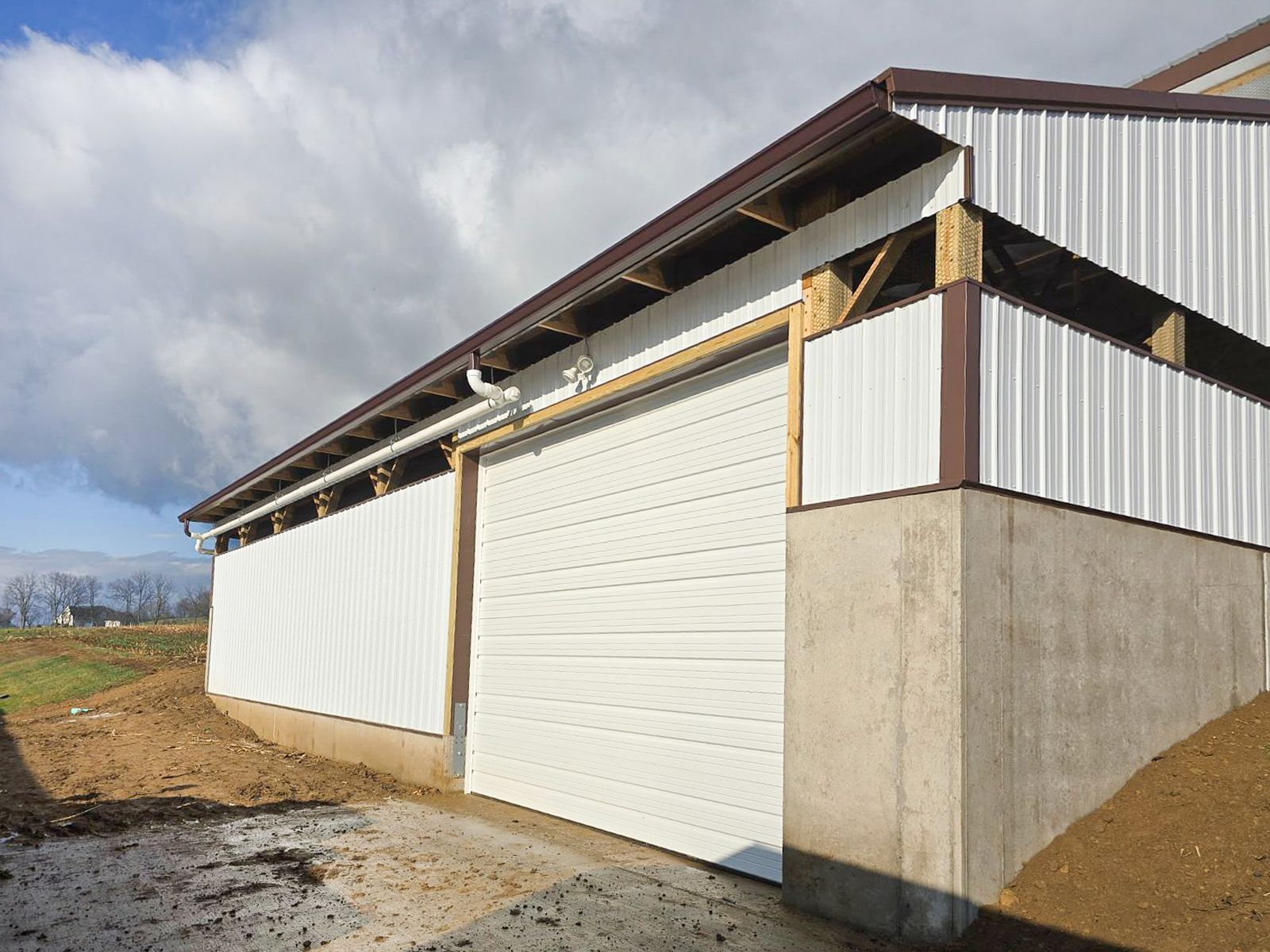 White industrial barn with large sliding doors and corrugated metal siding on a concrete foundation under cloudy skies