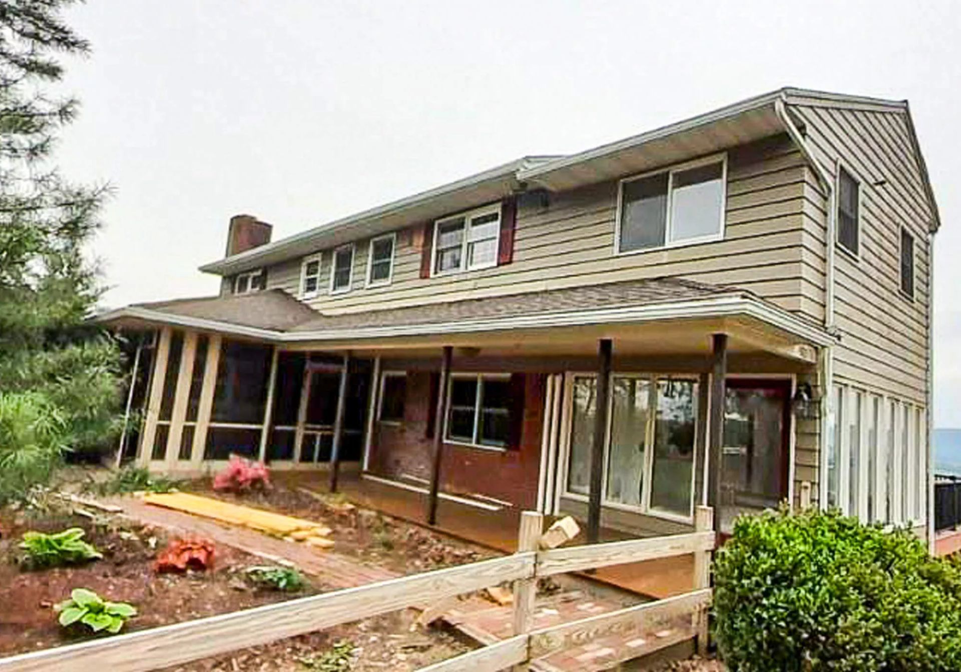 Two-story house with new siding and porch under construction, surrounded by landscaping and a wooden fence