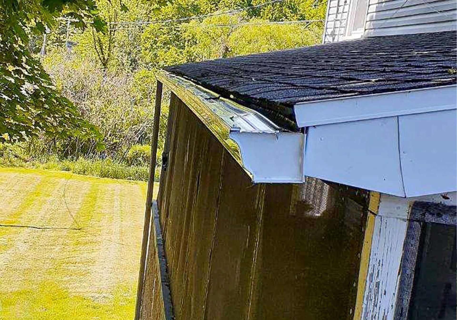 White house eave and dark wooden fence beside a sunlit grassy yard and trees