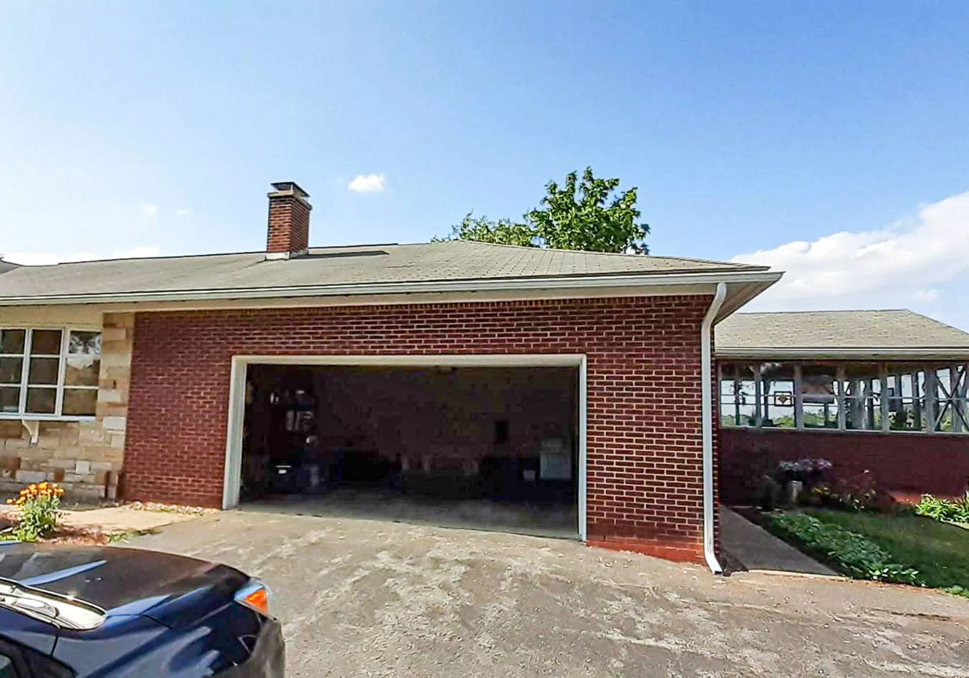 Brick house with open garage, driveway, and blue car under a clear sky