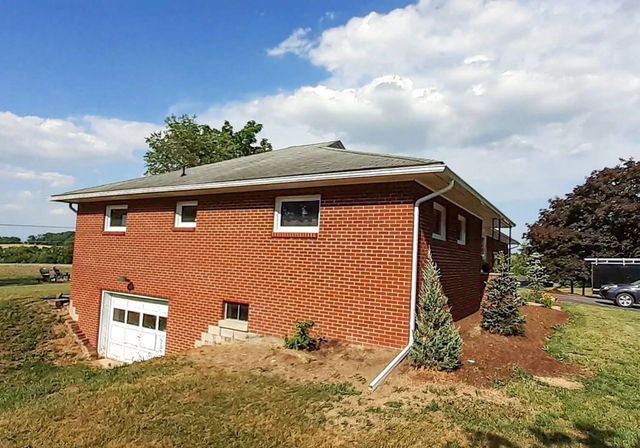 Brick house with a damaged lower wall and basement door, seen from a grassy yard under a cloudy sky