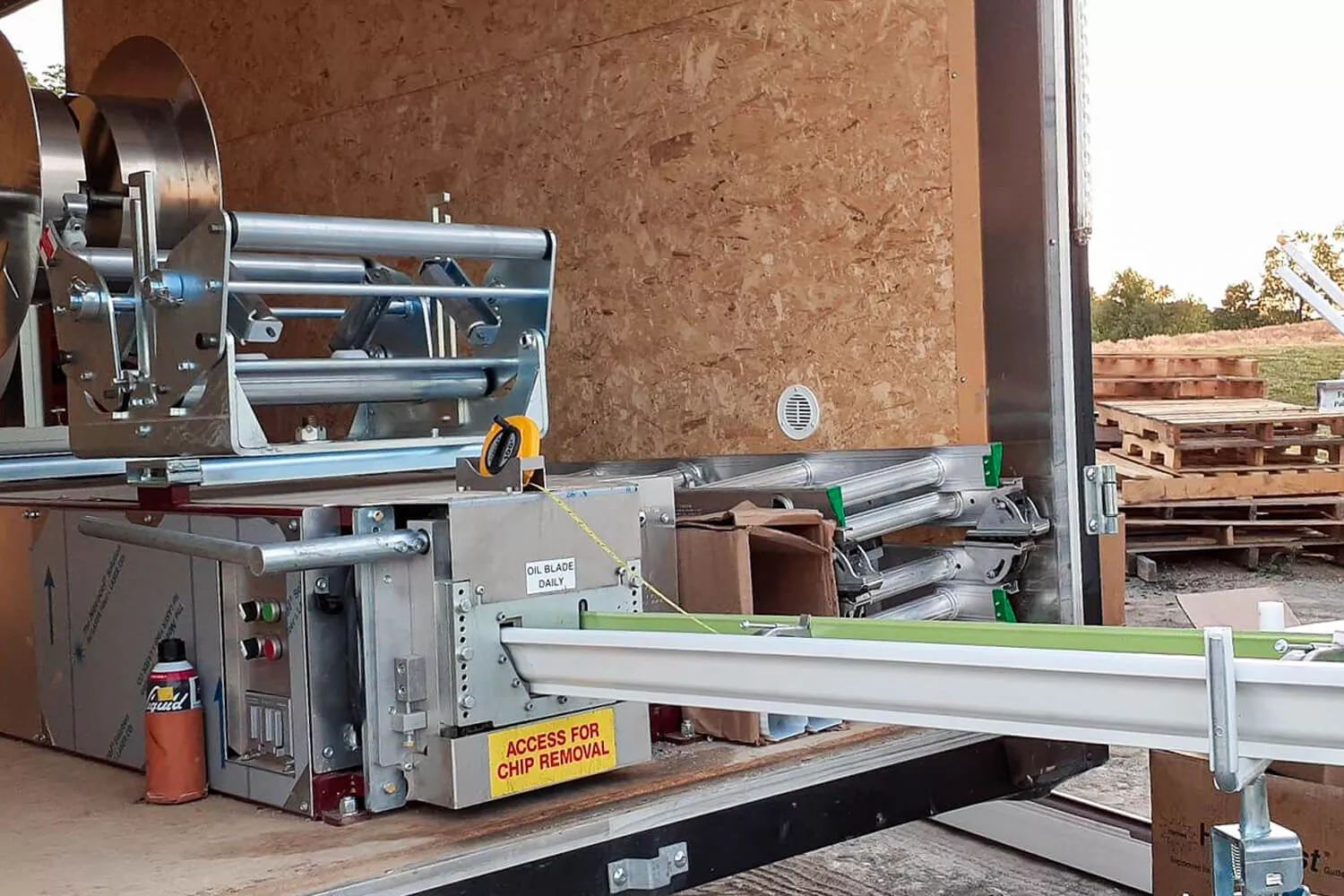 Industrial machine setup on a workbench with metal rollers, tools, and a white conveyor arm in a workshop.