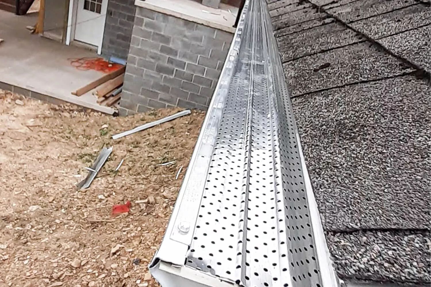 Roof gutter cleaning setup on a house roof beside a brick wall and gravel ground