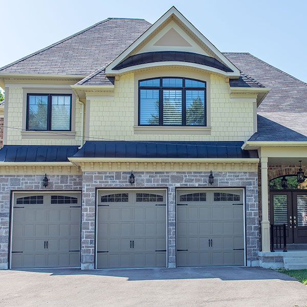 Two-story beige house with three garage doors and a stone-and-shingle exterior