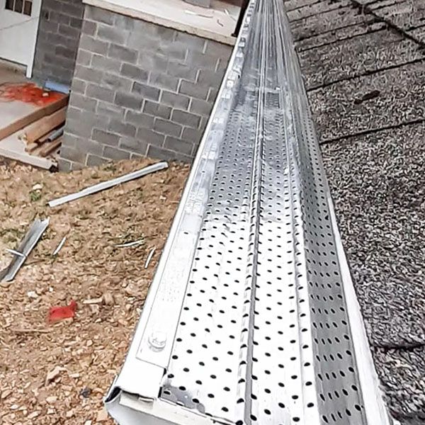 Perforated metal gutter on a roof edge beside a brick wall and construction debris below