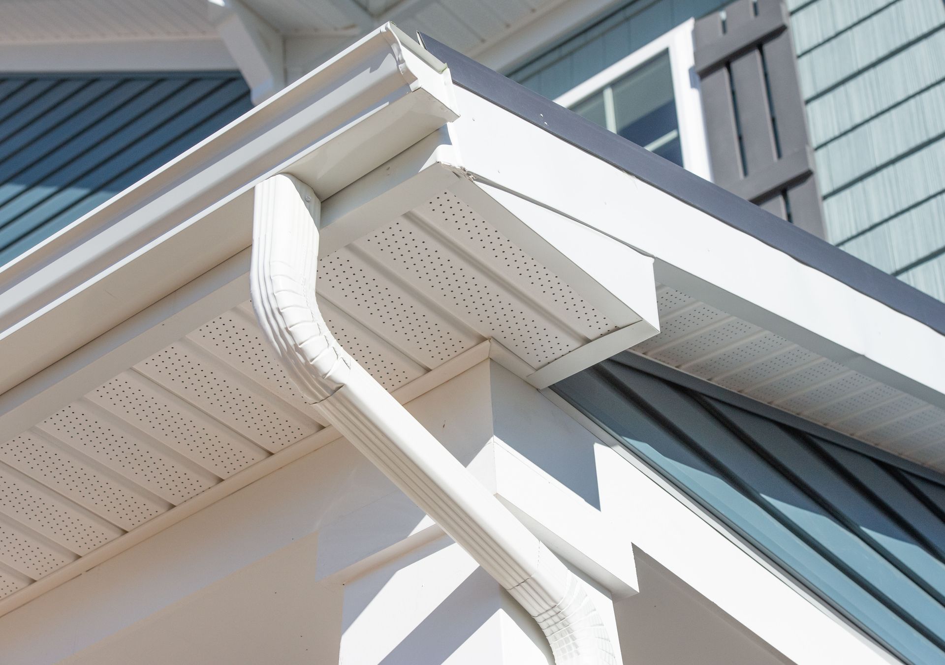 Close-up of a white house roof eave with gutter and blue siding against the sky