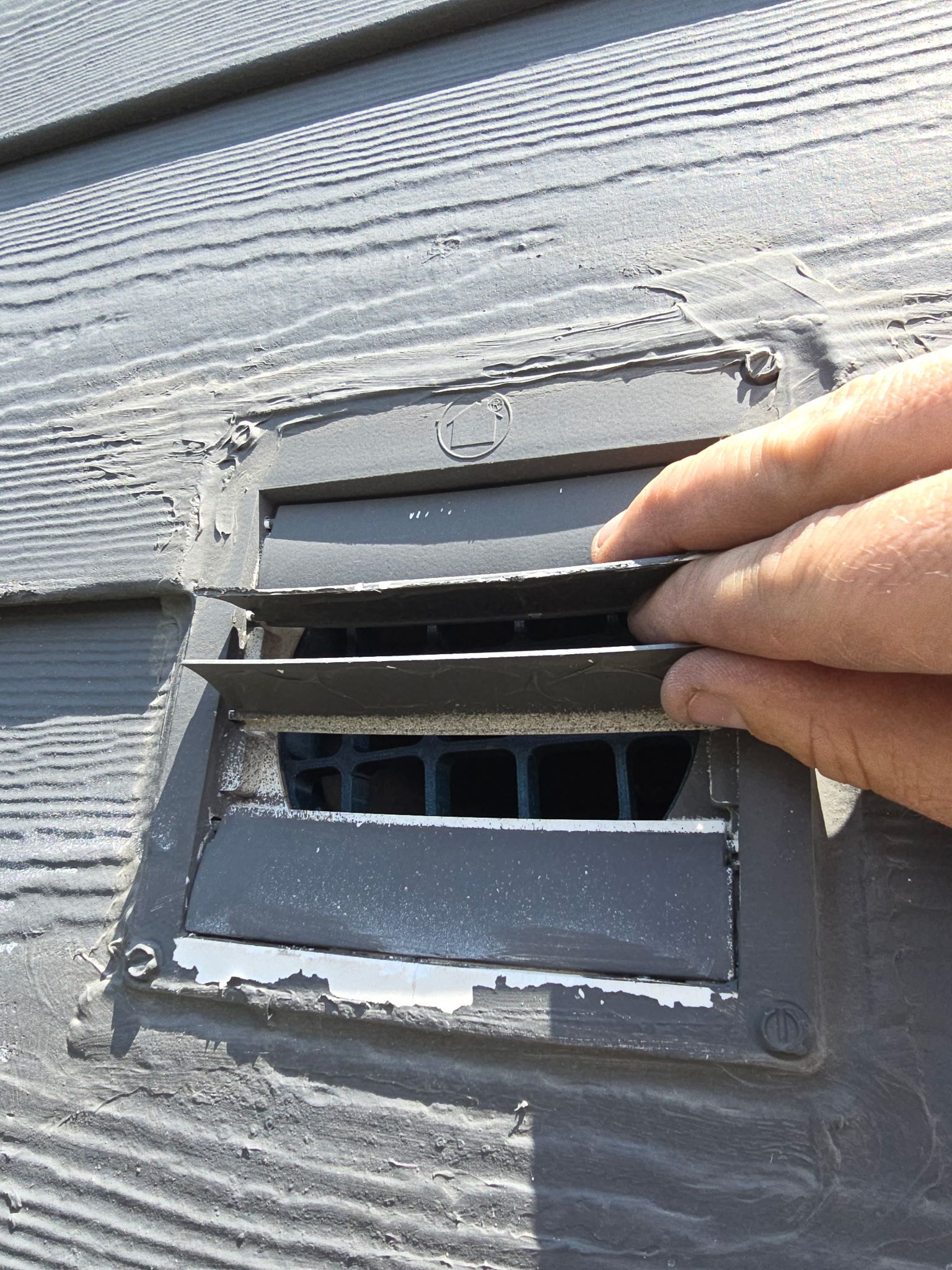 A person is opening a vent on the side of a building