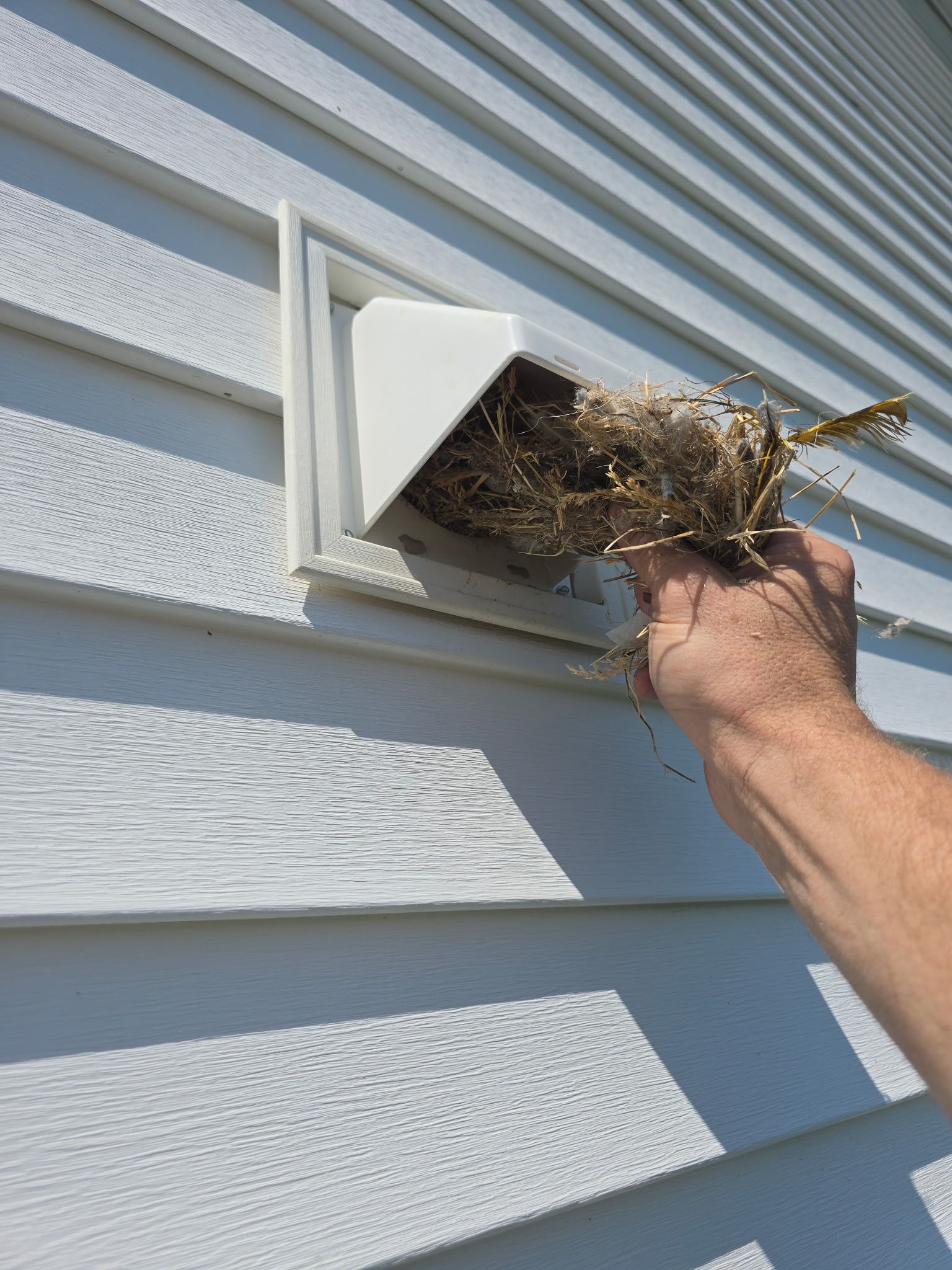 A person is cleaning a vent on the side of a house