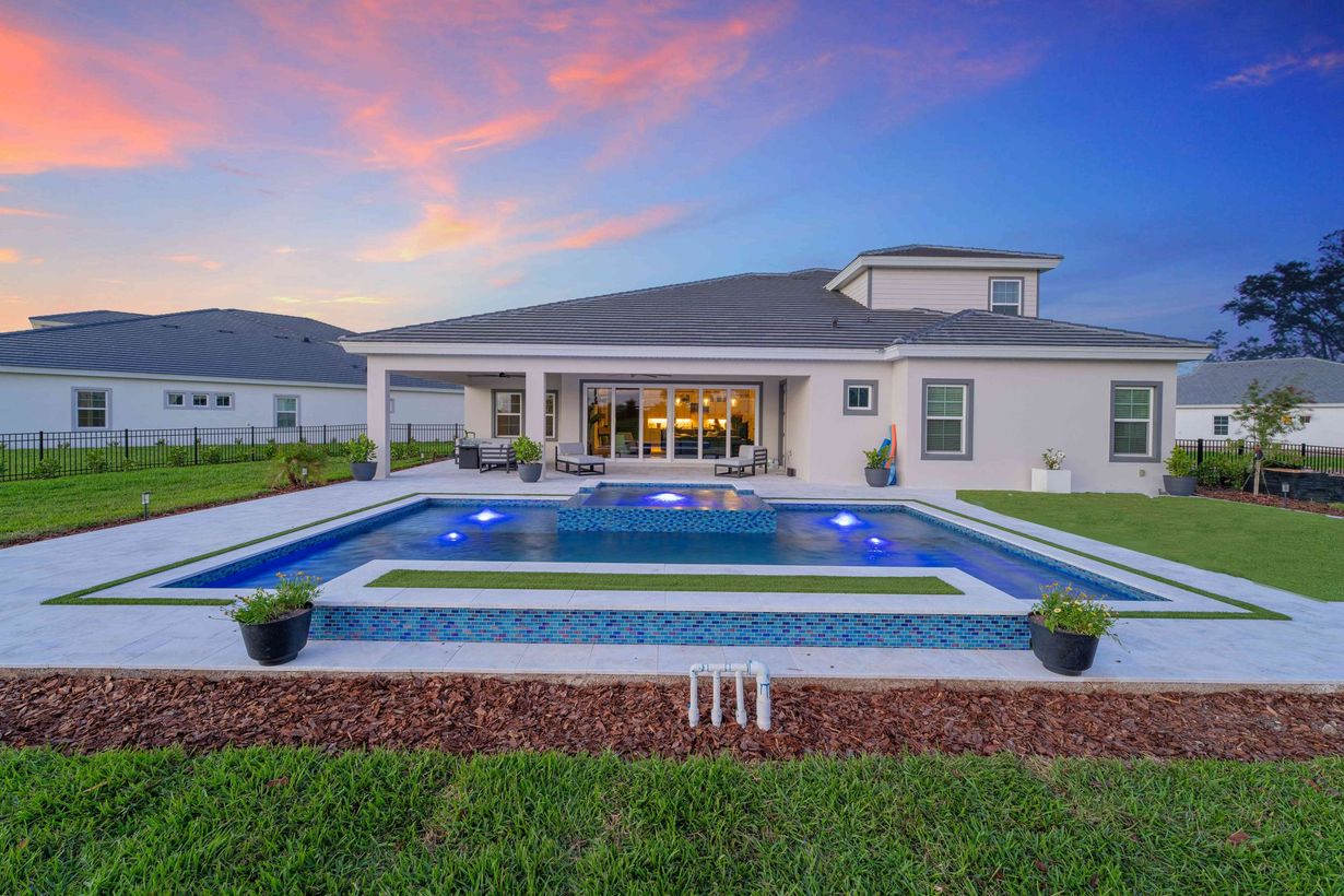 Modern white house with a lit pool and landscaped yard at sunset