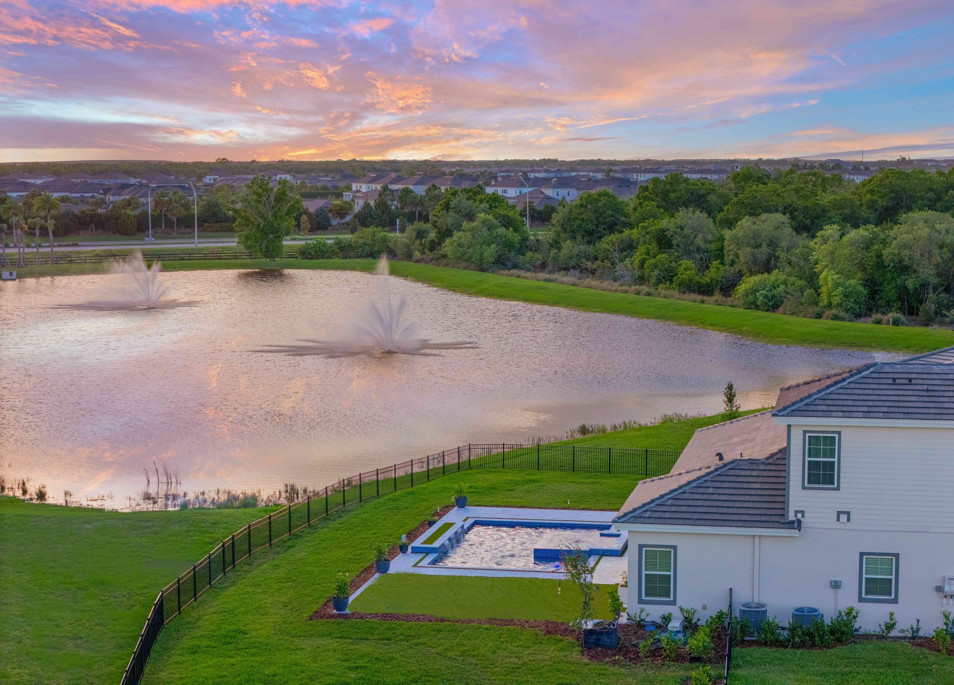 Sunset over a pond beside a white house, with a green lawn and small swimming pool in the foreground