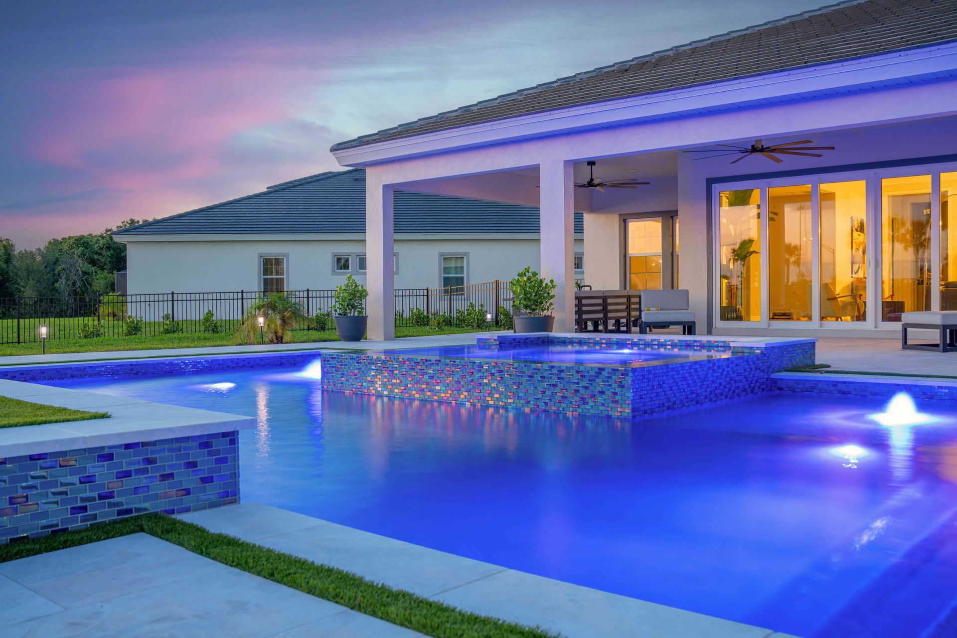 Modern house with lit pool and patio at dusk, reflected blue water and warm indoor lights.