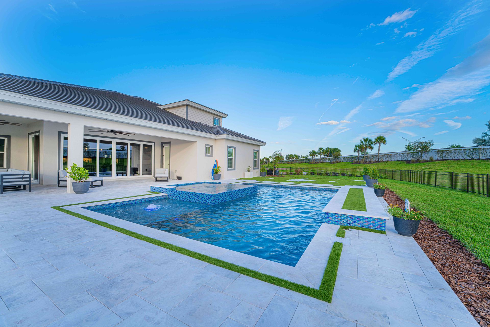 Modern backyard with a blue swimming pool beside a white patio and green lawn under a clear sky