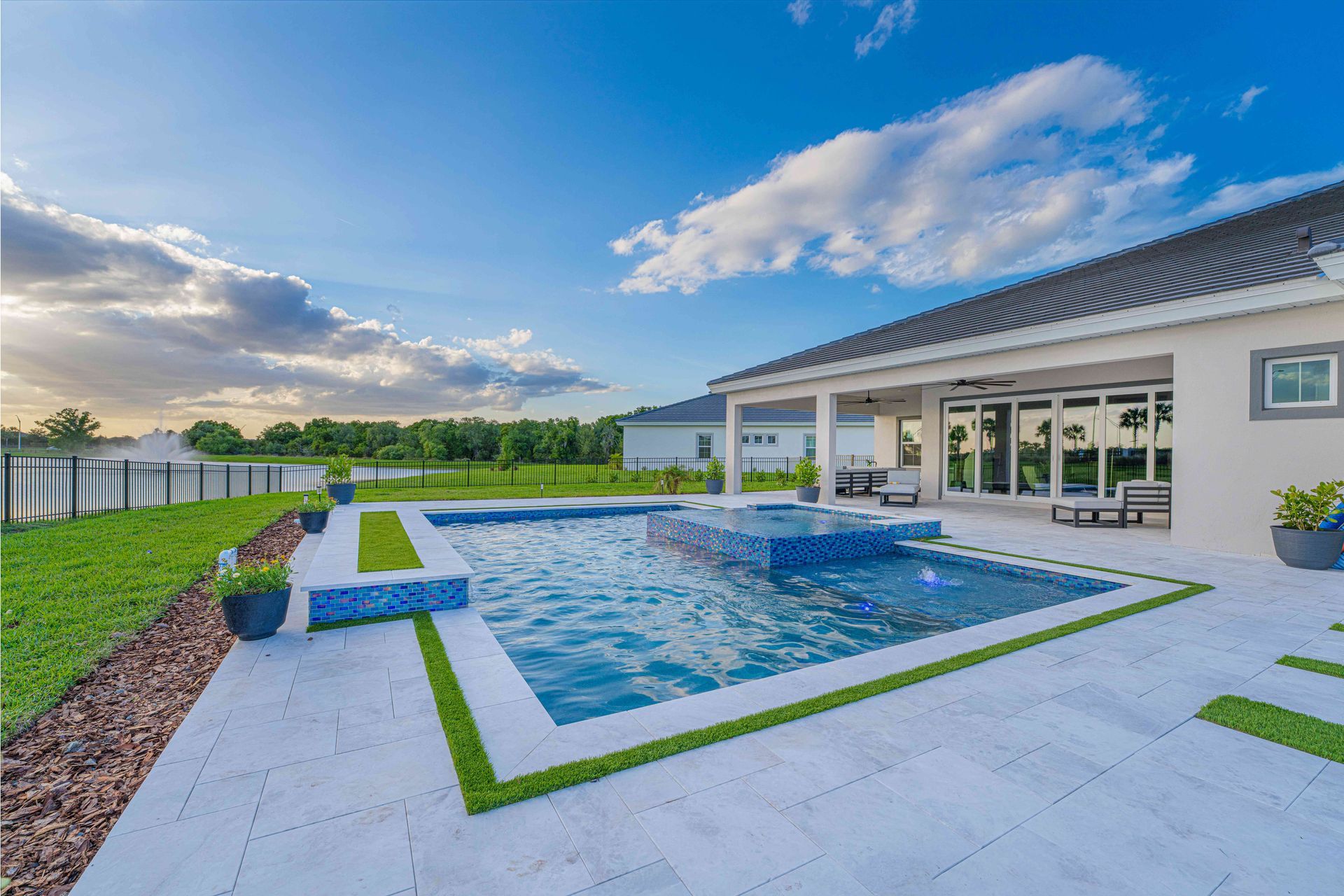 Modern backyard with a blue-tiled pool, patio, and white house under a sunny sky