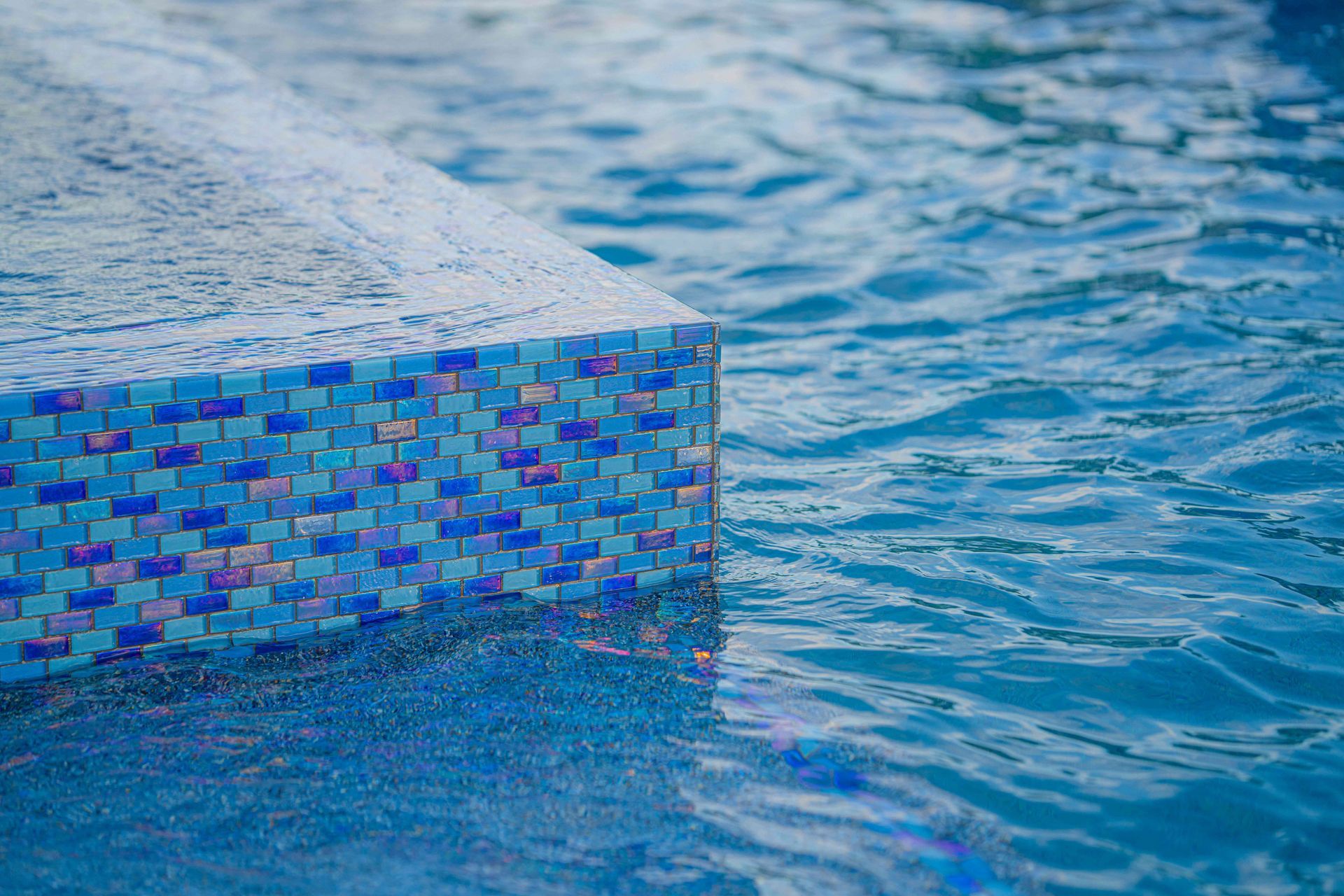 Blue mosaic-tiled pool edge beside rippling blue water