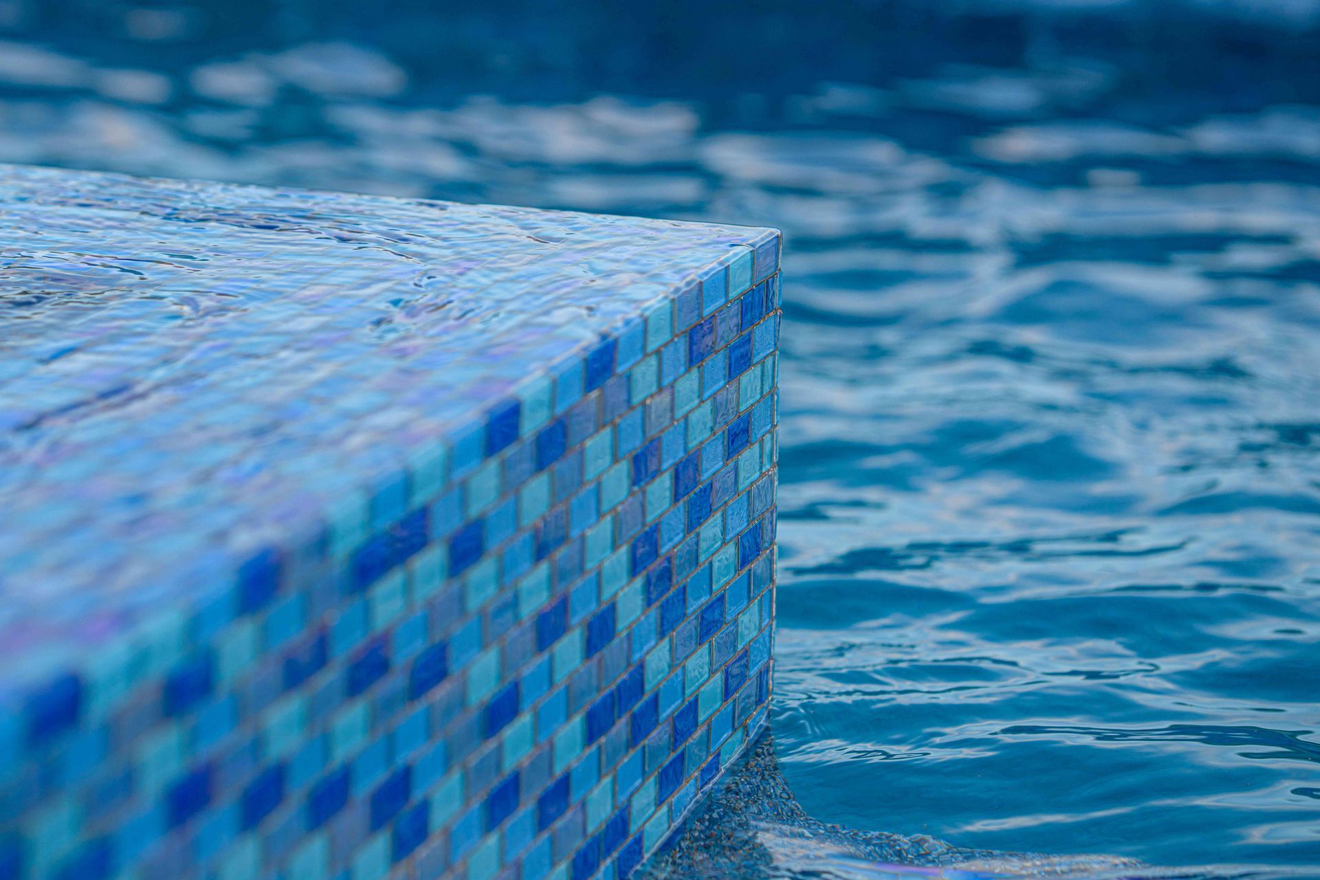 Blue mosaic pool edge beside rippling water