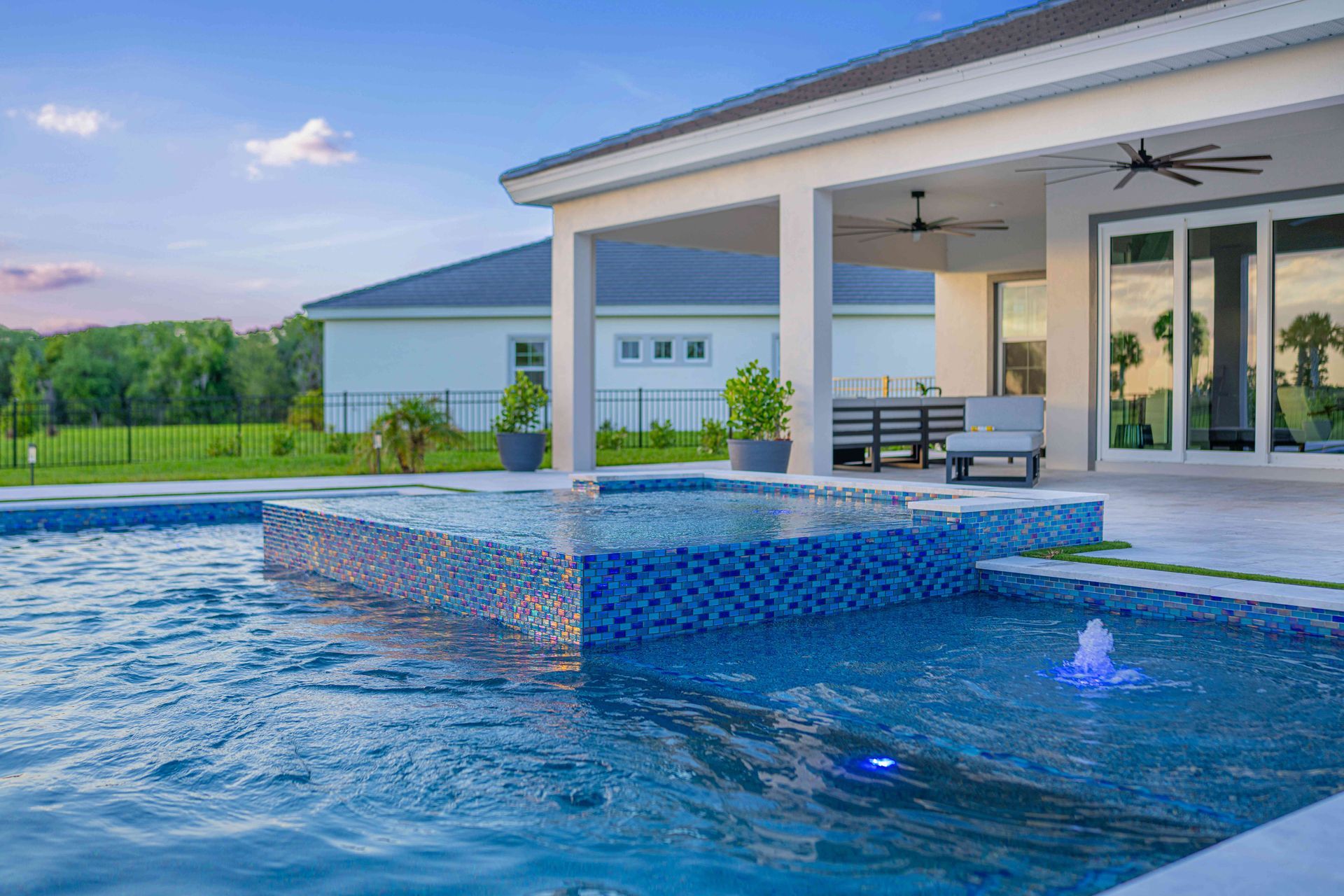 Backyard pool with a raised blue-tiled spa and covered patio beside a modern house