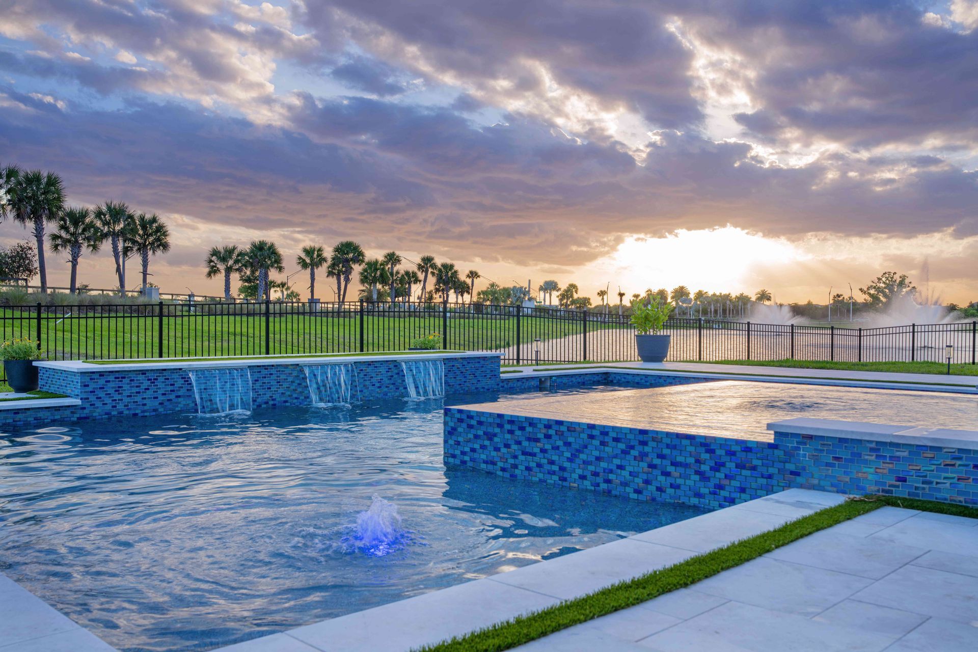 Infinity pool at sunset with blue water, tiled deck, palm trees, and cloudy sky