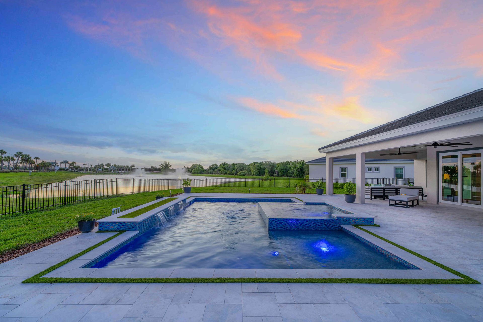 Modern backyard with lit pool, manicured lawn, and covered patio at sunset