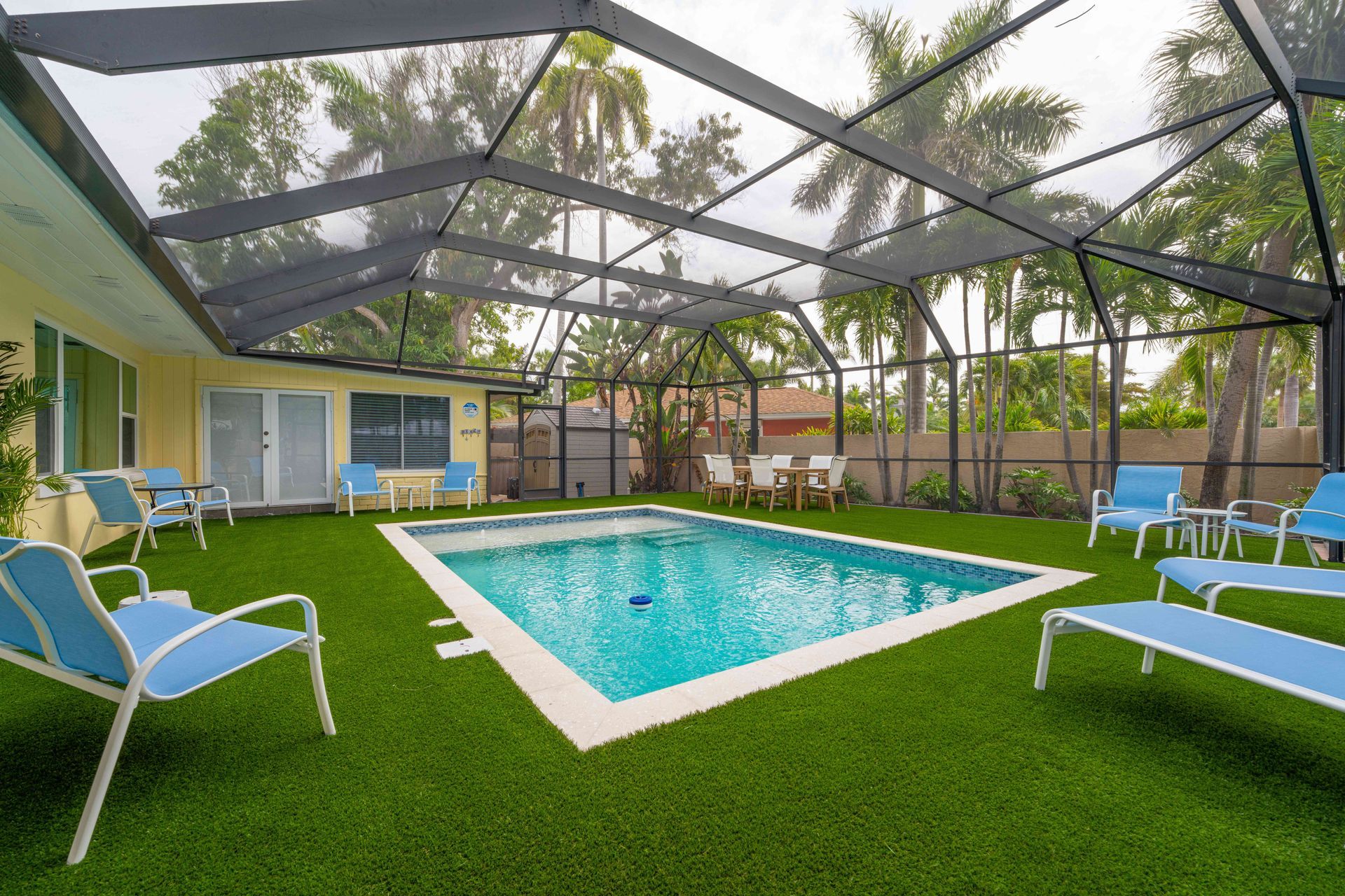 Backyard pool with blue lounge chairs under a screened patio beside a house