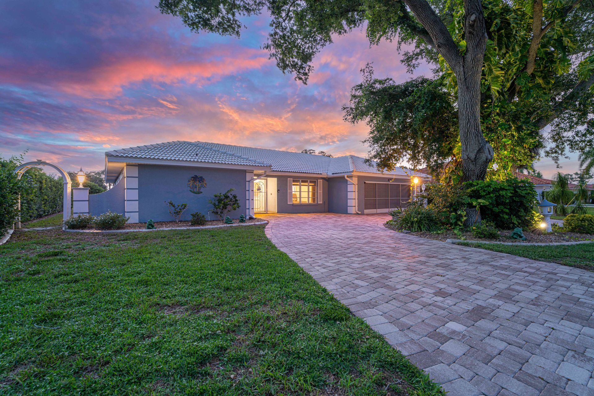 Single-story house with lit windows, driveway, and front lawn at sunset