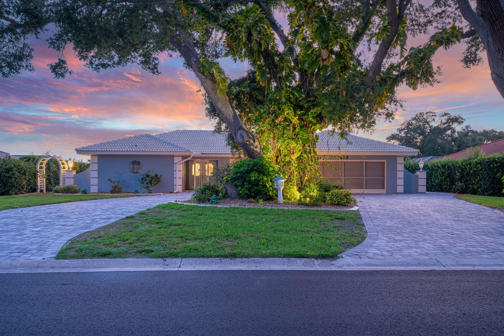 Suburban house with two garages, large tree in front yard, and pink sunset sky