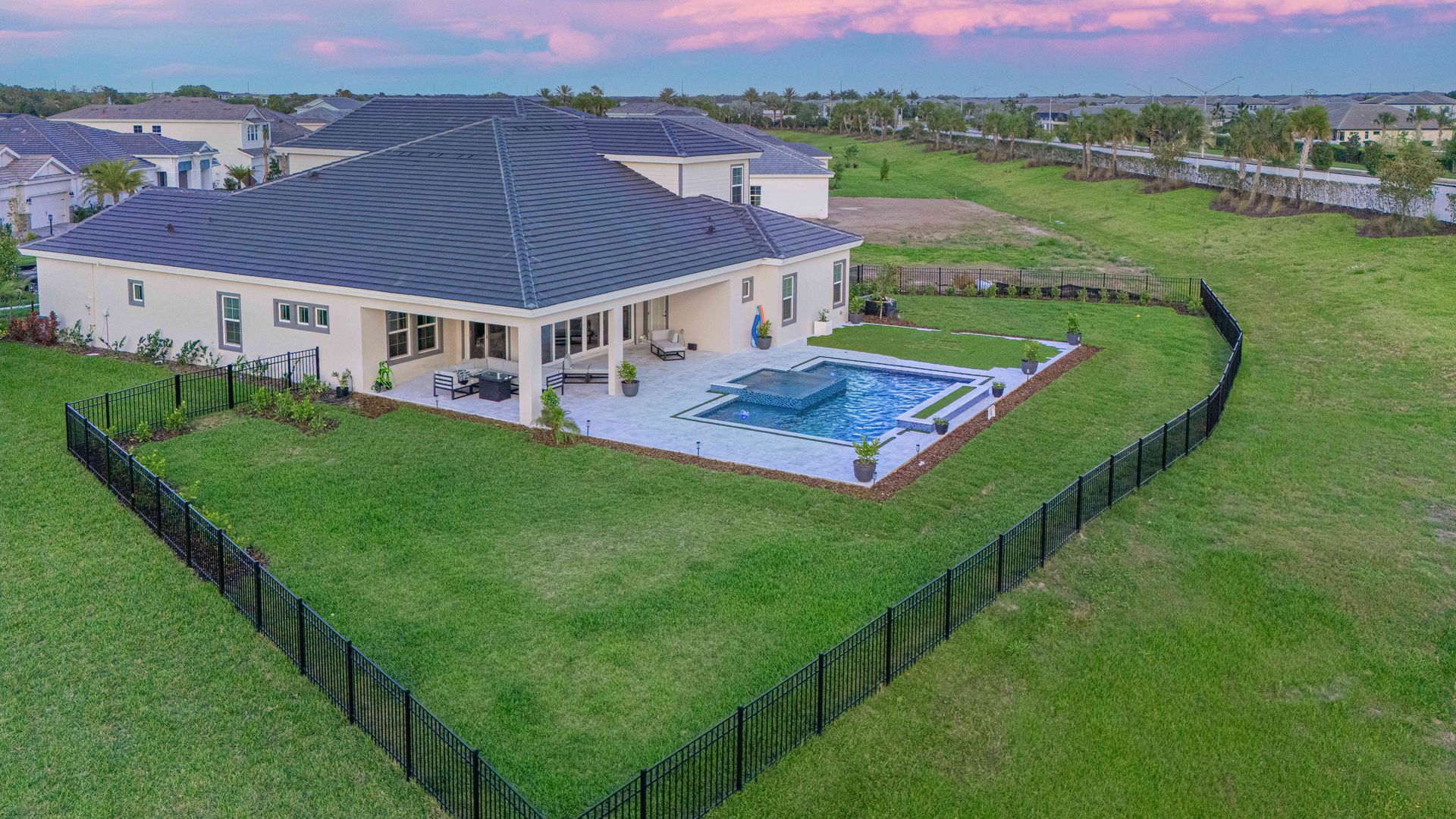 Aerial view of a modern house with a fenced green lawn and a backyard pool at sunset