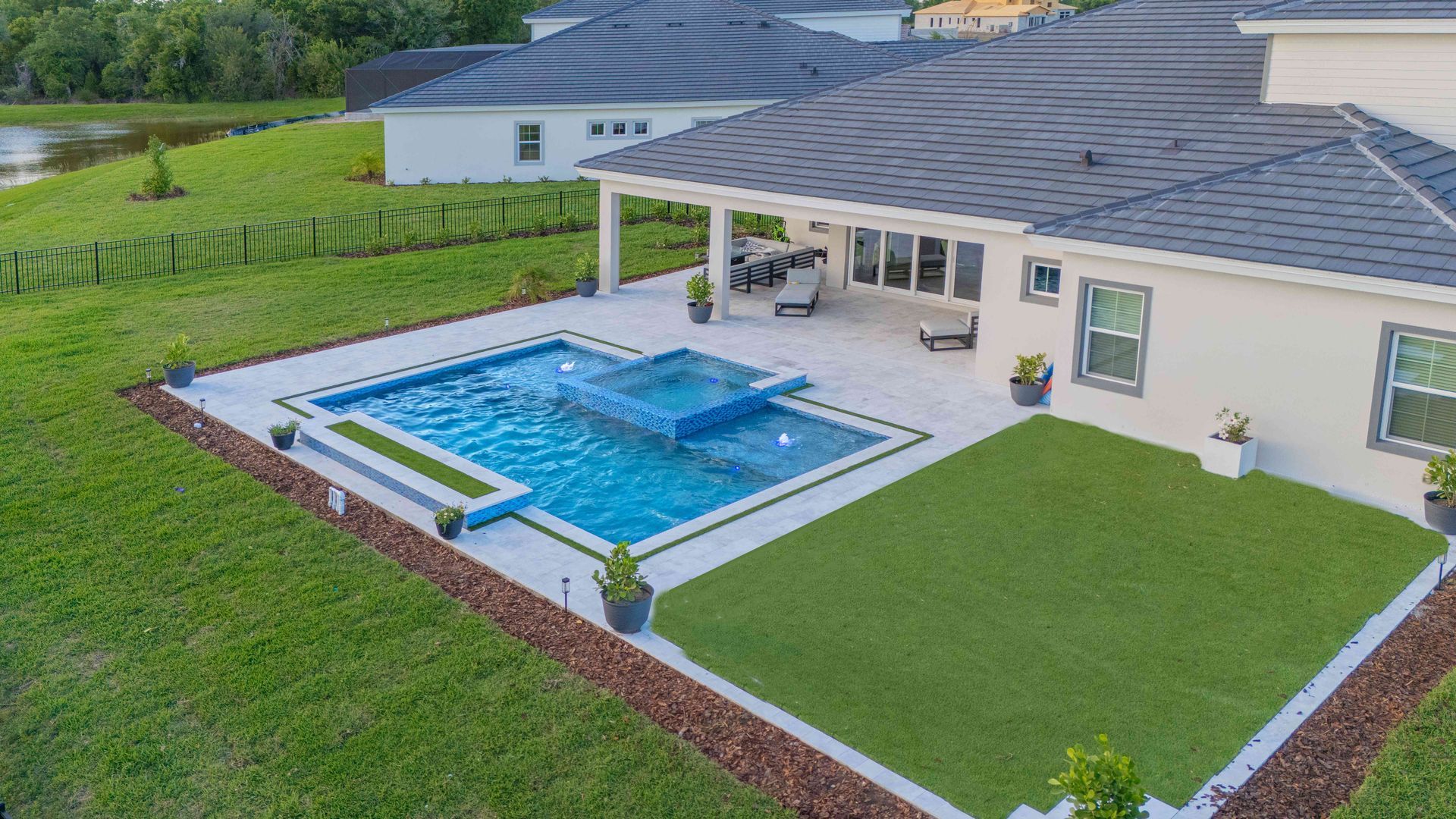 Backyard patio with a blue swimming pool beside a beige house and green lawn
