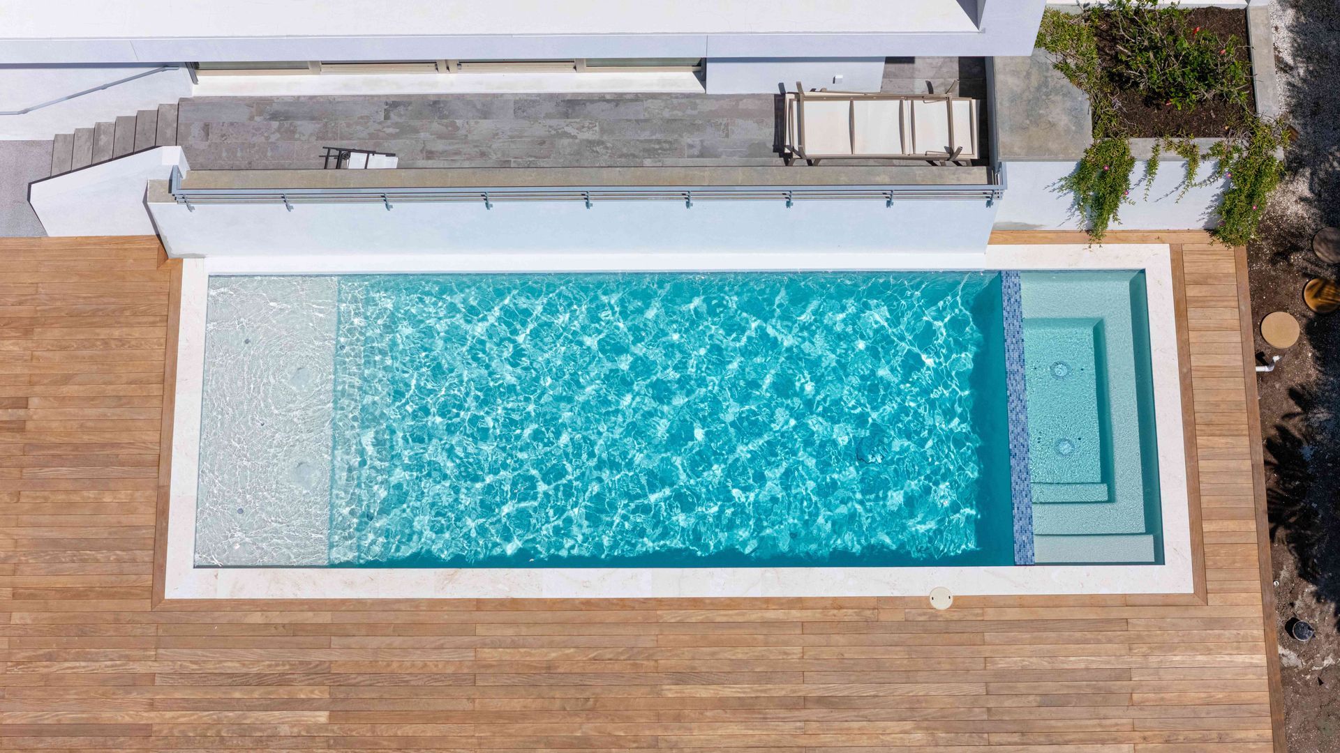 Top-down view of a rectangular turquoise pool beside a wooden deck and white lounge area.