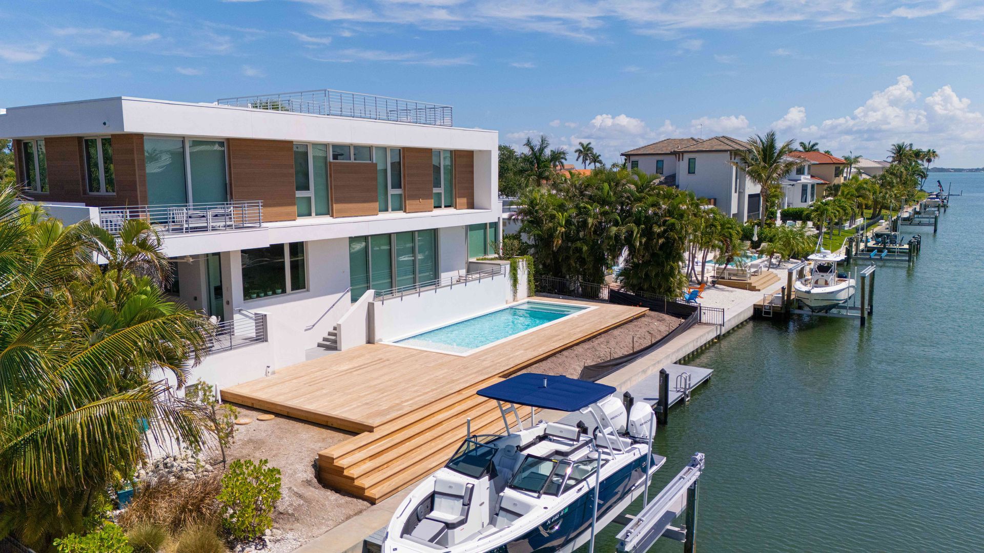 Modern waterfront villa with pool, patio lounge chairs, and docked boats beside a canal