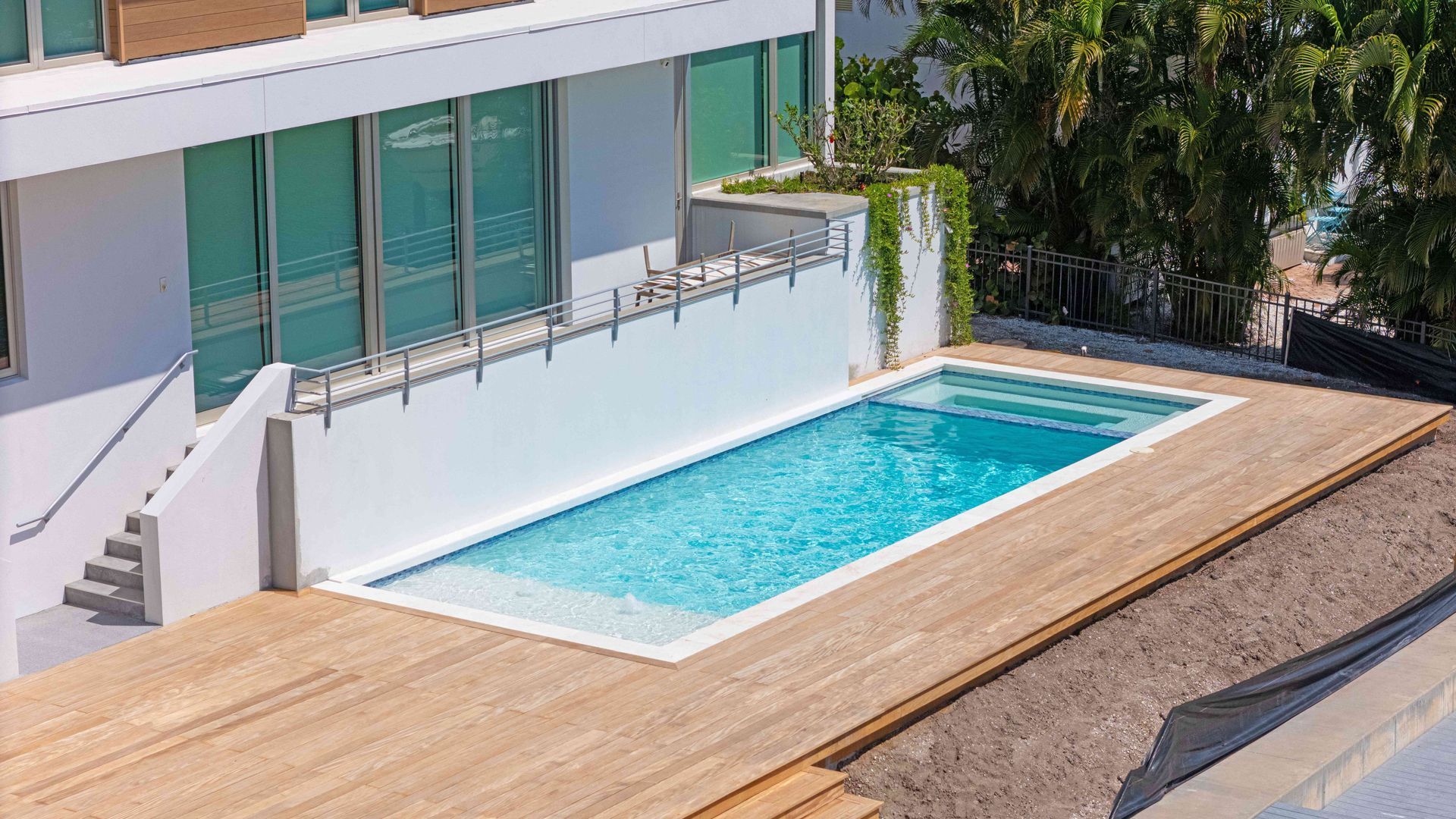 Modern house patio with a rectangular blue swimming pool and wooden deck railing