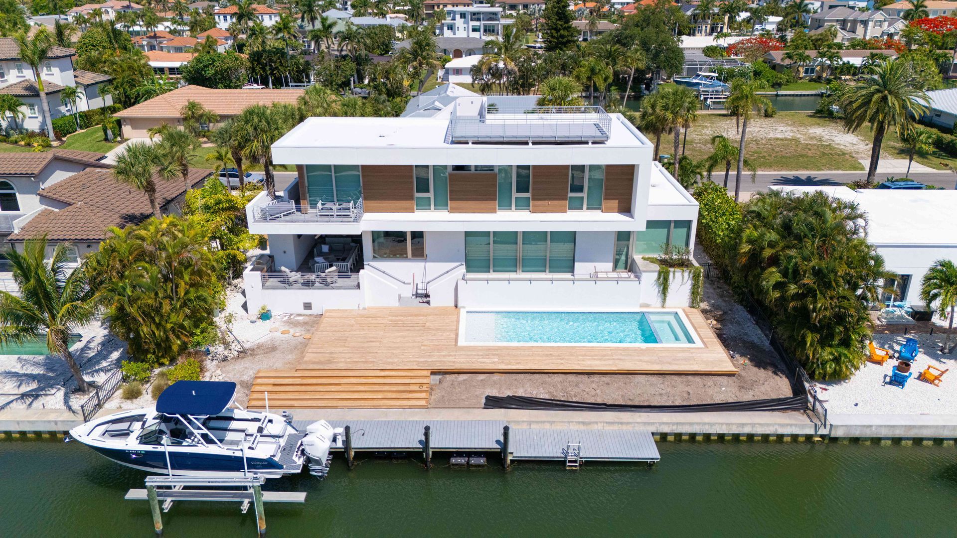 Modern waterfront house with pool, wooden deck, and docked boat by the canal