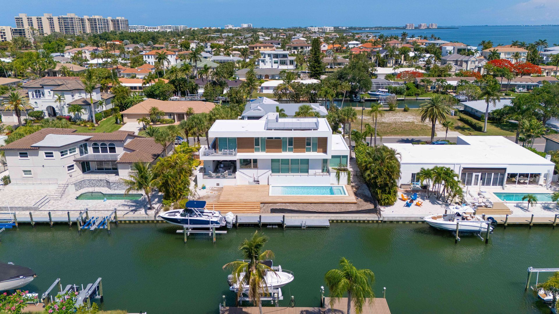Aerial view of waterfront homes along a canal with boats, docks, and palm trees.