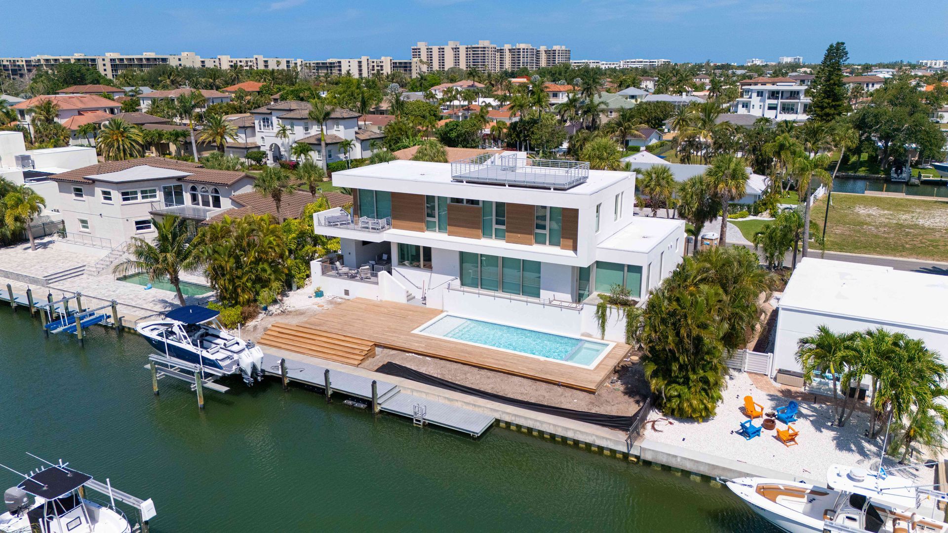 Modern waterfront home with a dock, pool, and boats along a canal under a sunny sky