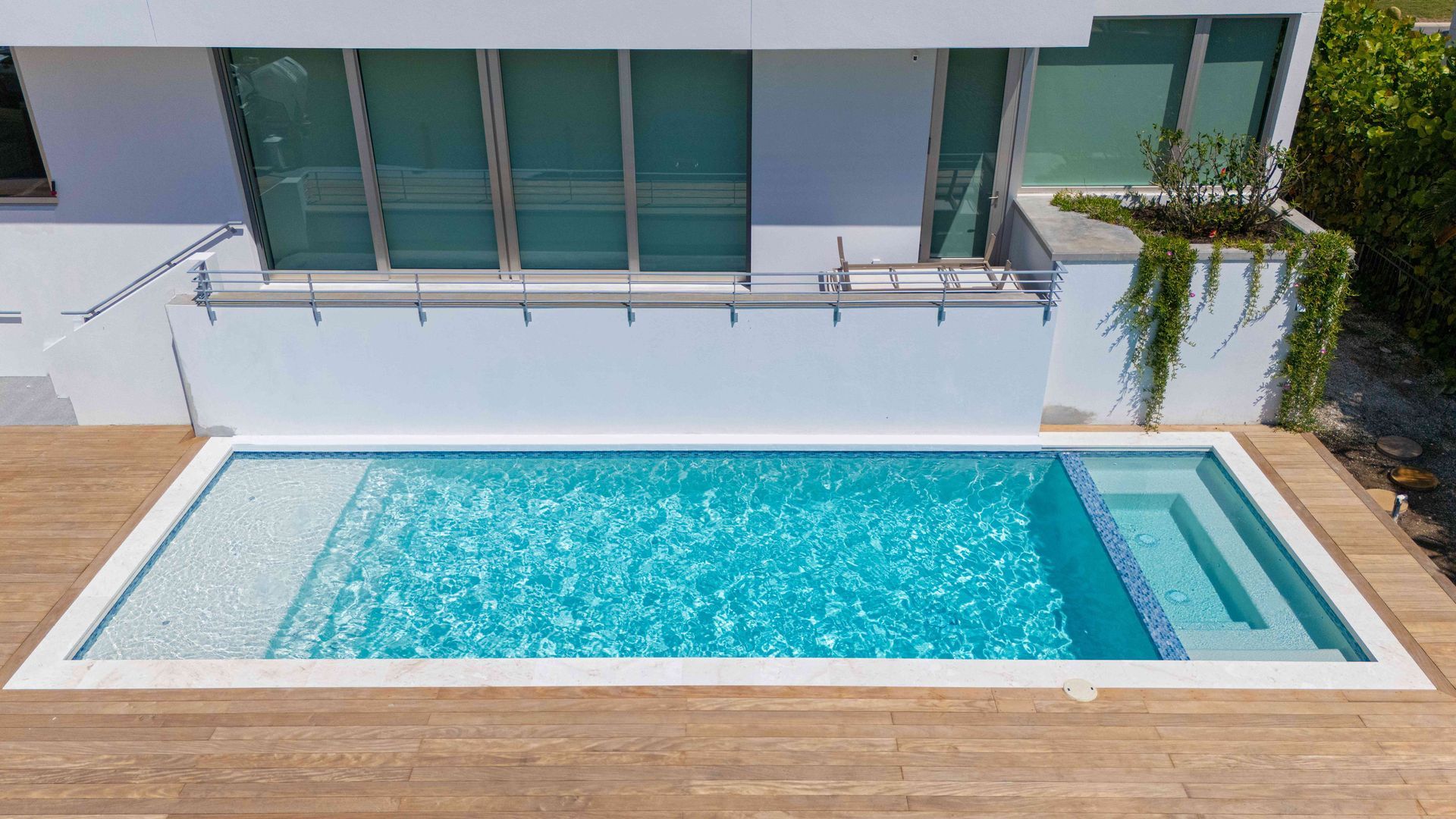Rectangular backyard pool with turquoise water beside a modern house and wooden deck