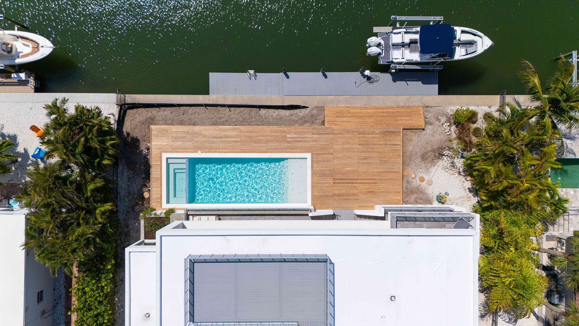 Aerial view of a rooftop pool and deck beside a canal with a small boat docked nearby.