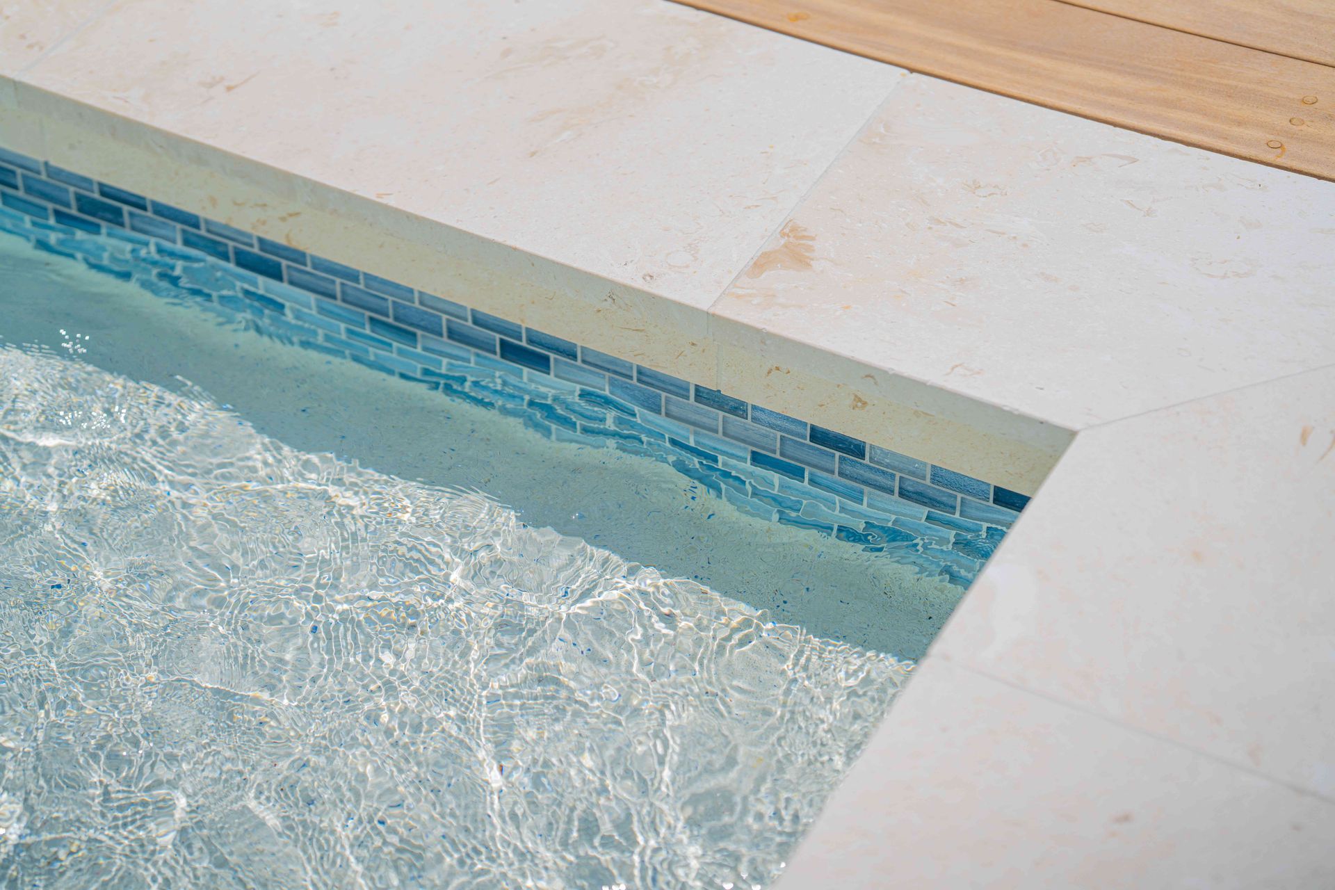 Pool edge with blue tile border beside rippling water and light stone deck