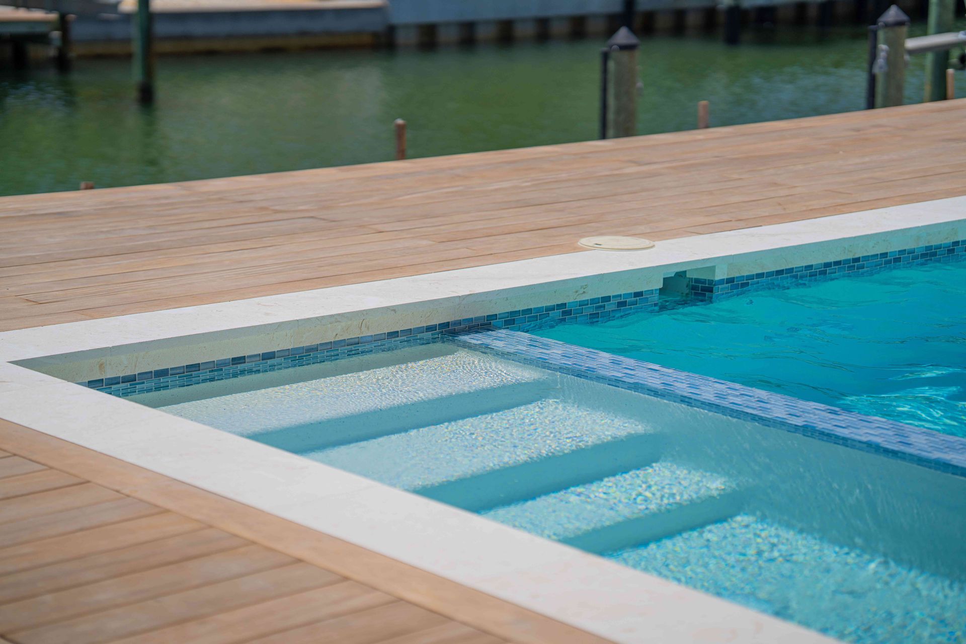 Outdoor swimming pool with shallow steps, blue water, and a wooden deck around it