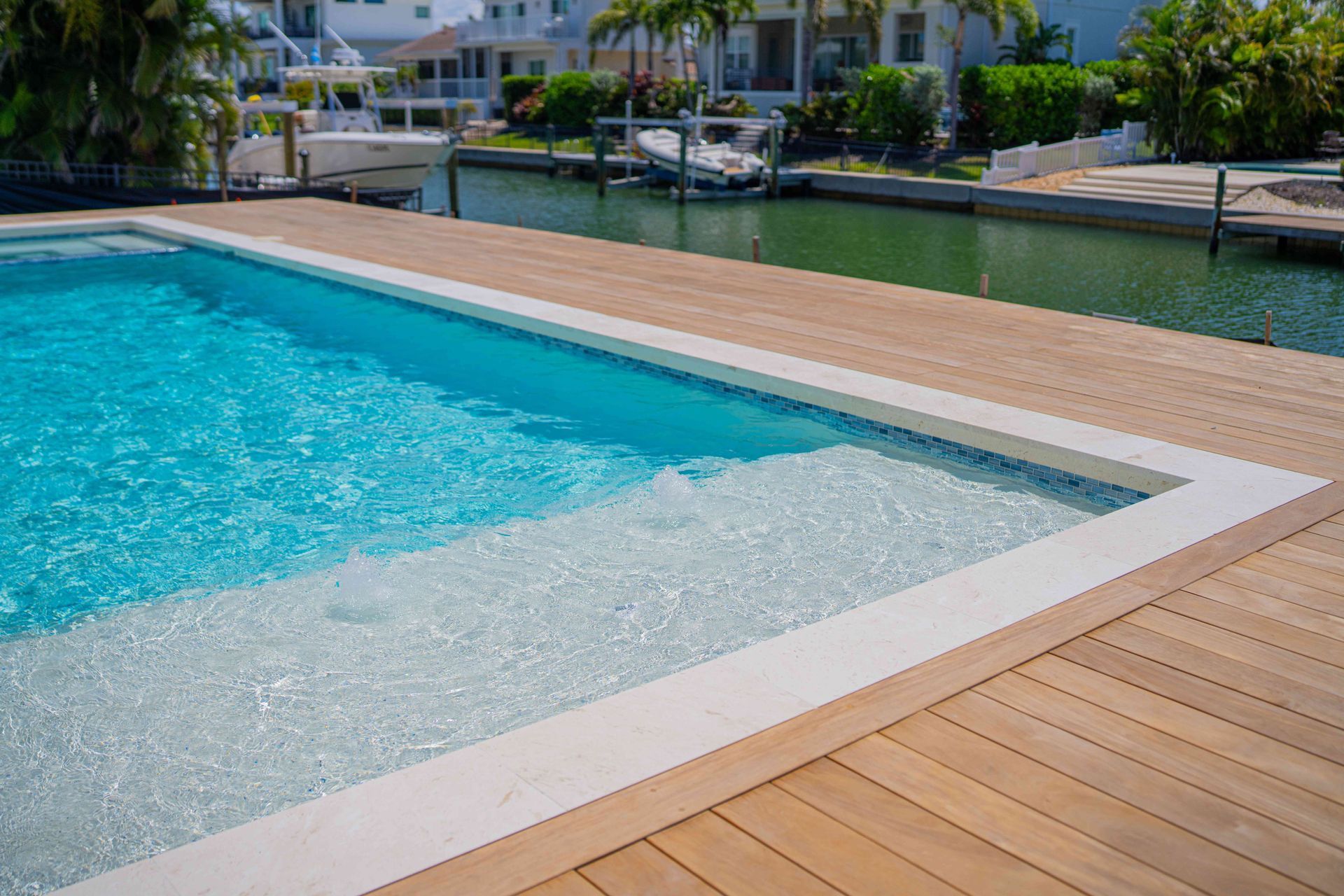 Infinity pool beside a waterfront deck with palm trees and boats in the background
