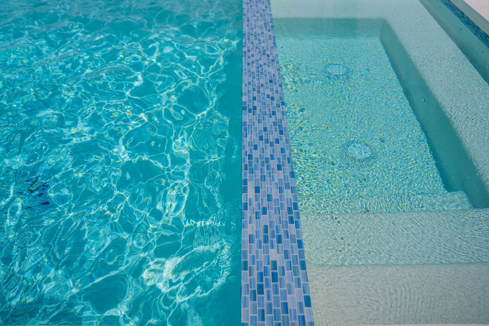 Blue mosaic pool edge beside a shallow spa or hot tub with clear turquoise water