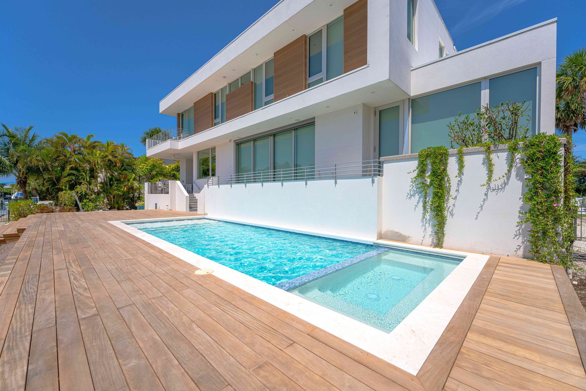 Modern white house with a wooden deck and rectangular swimming pool under a blue sky