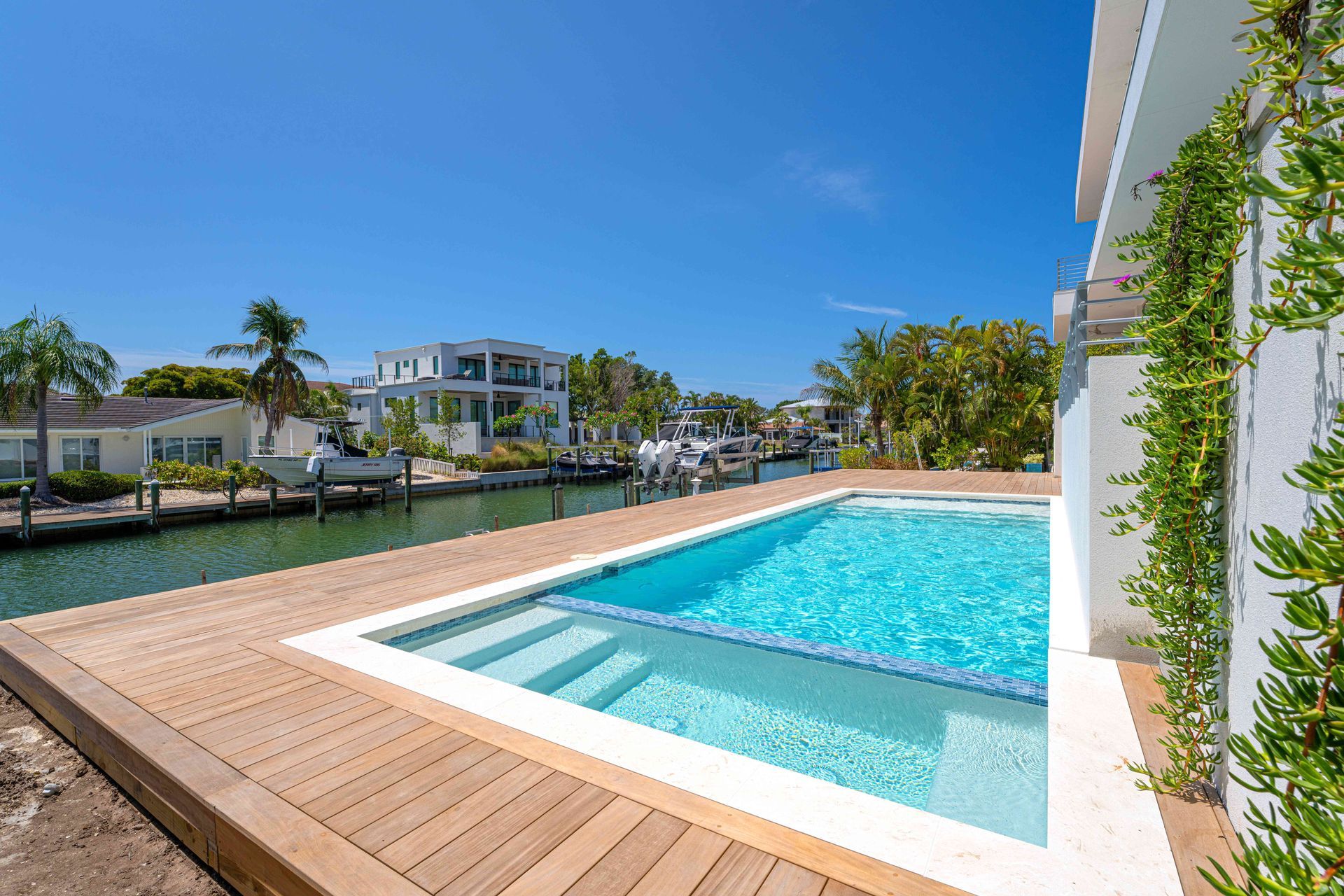 Modern poolside deck with a turquoise swimming pool, canal view, and blue sky