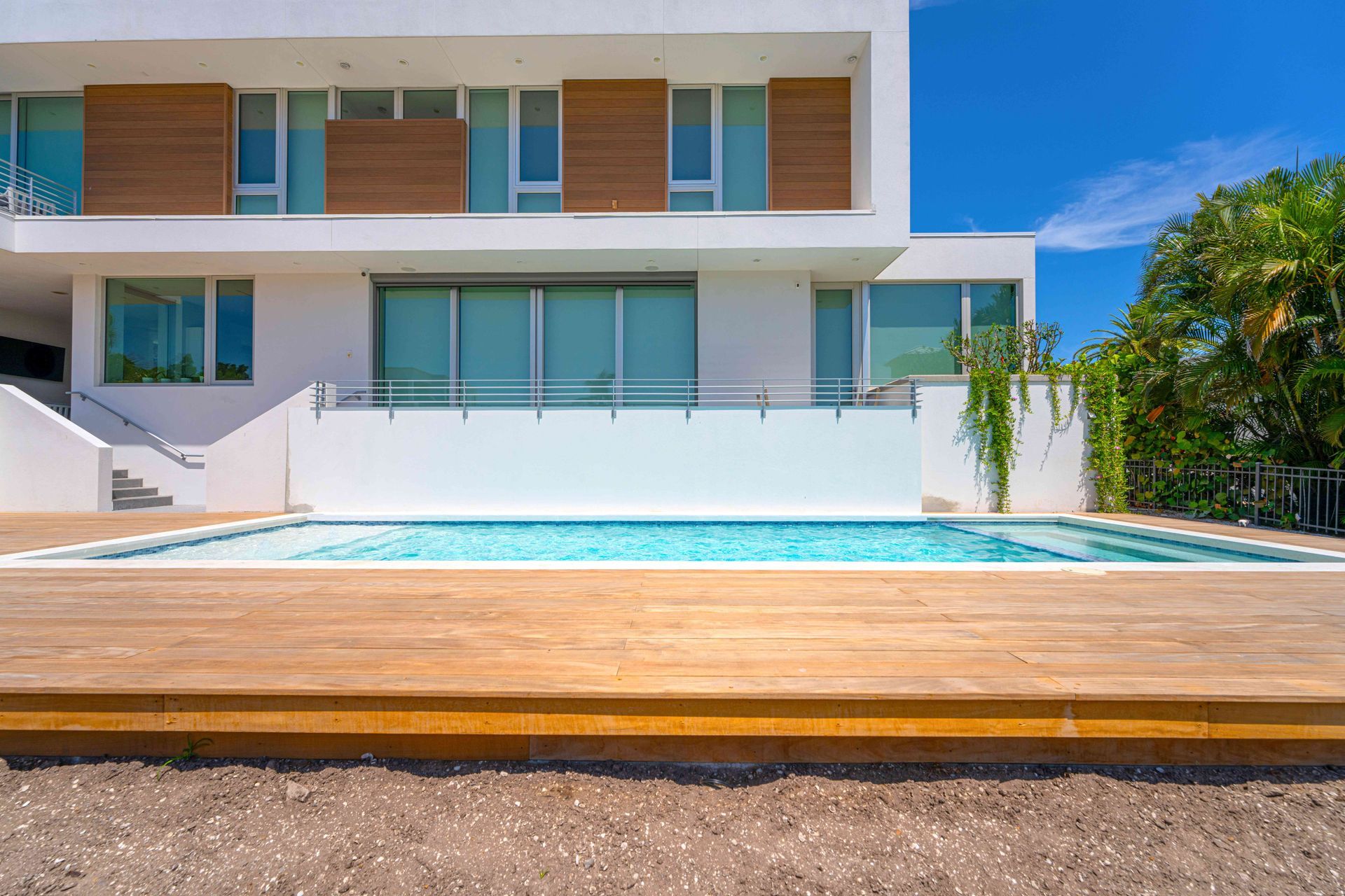 Modern white house with a turquoise pool and wooden deck under a clear blue sky
