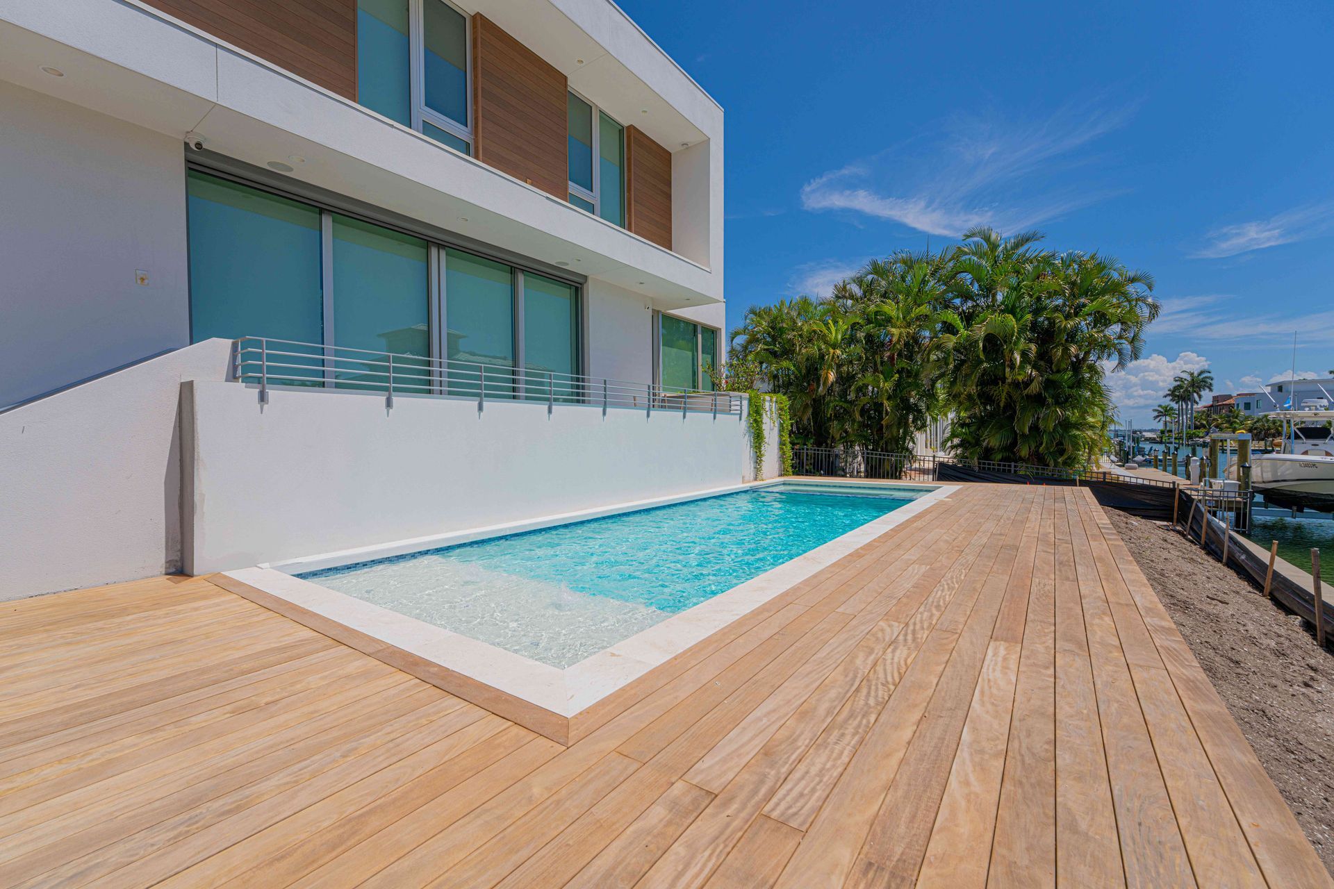Modern poolside patio with wooden deck beside a white house under a clear blue sky