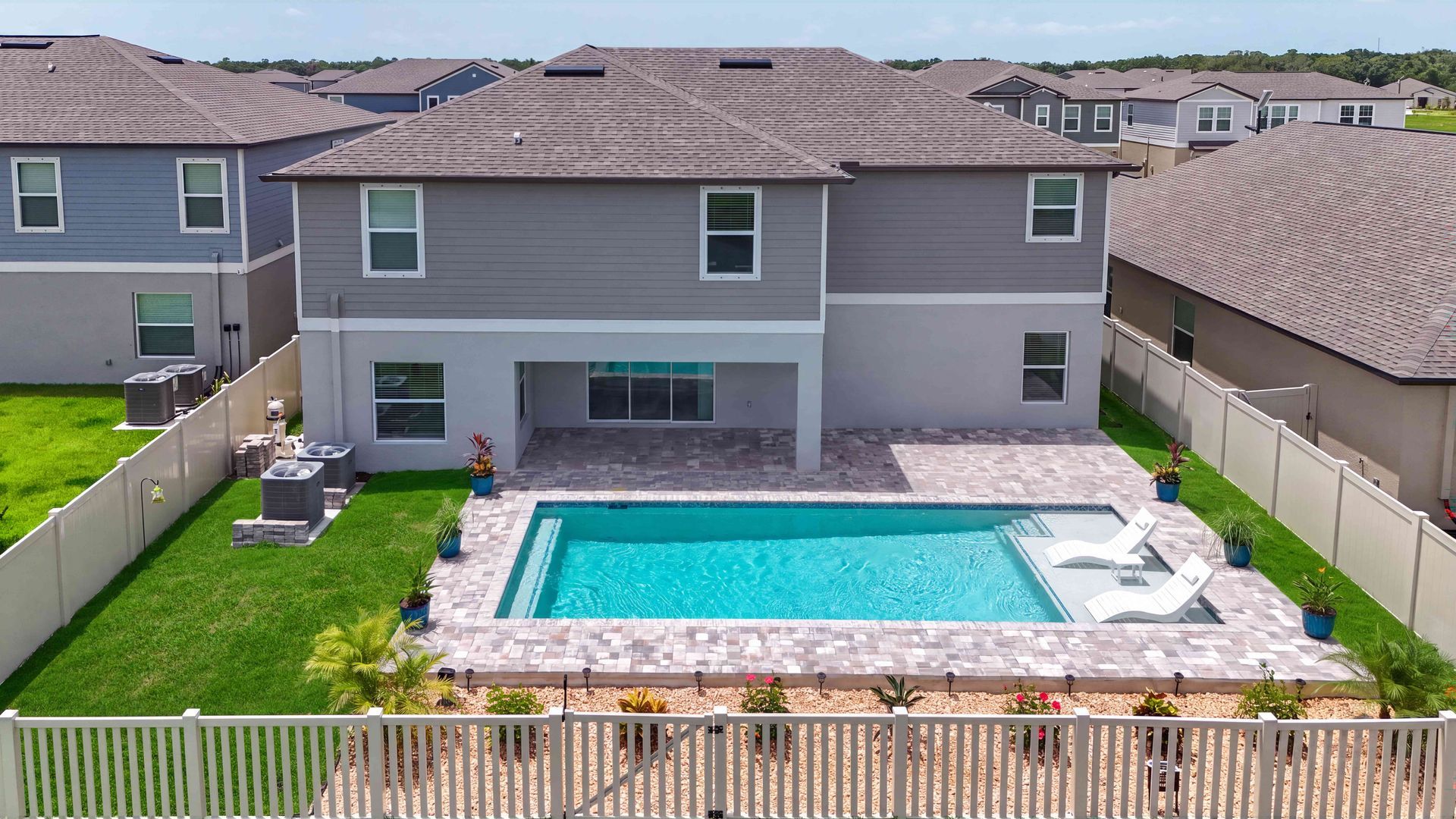 Backyard with a rectangular swimming pool behind a two-story house and fenced green lawn