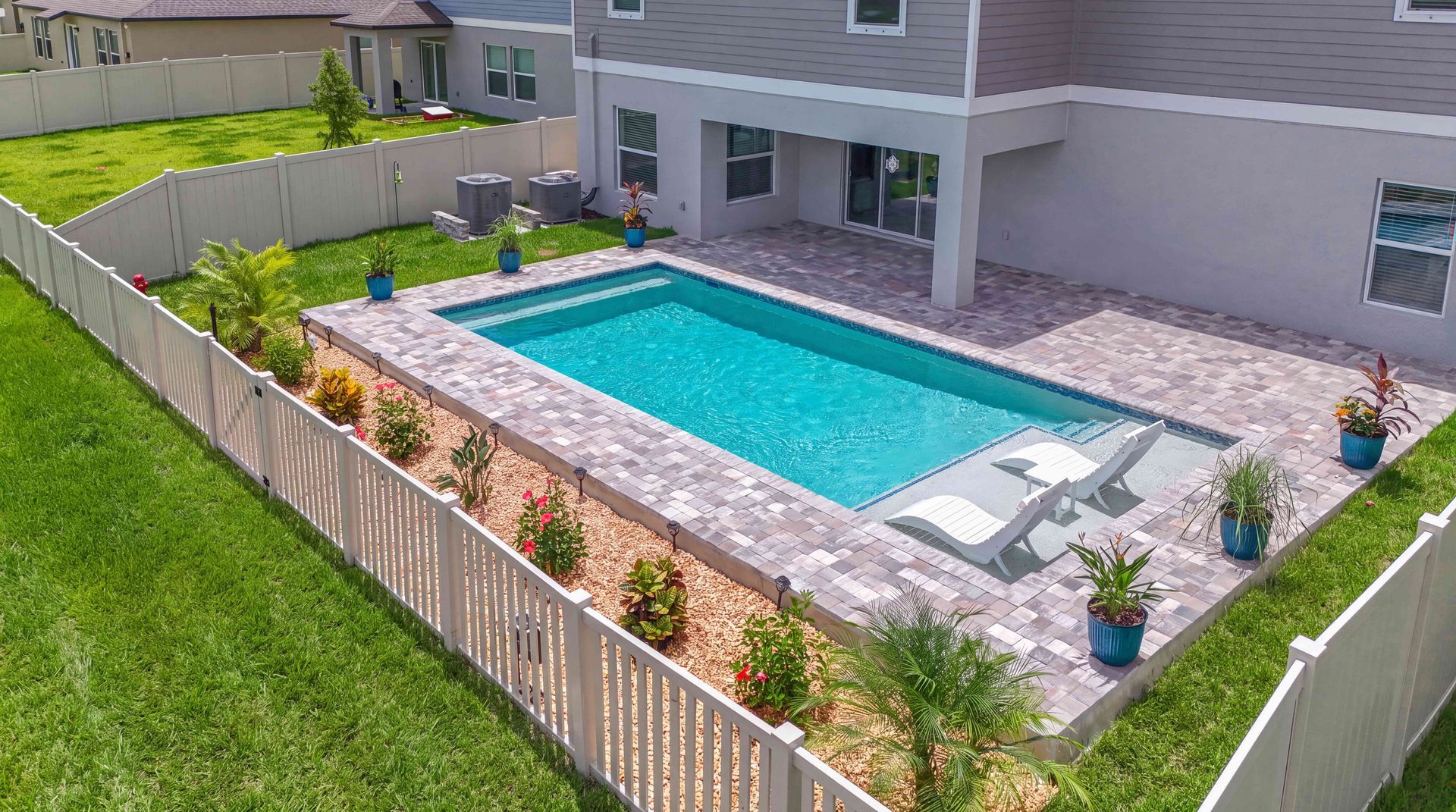 Backyard with a rectangular swimming pool, patio chairs, and landscaped fencing beside a house