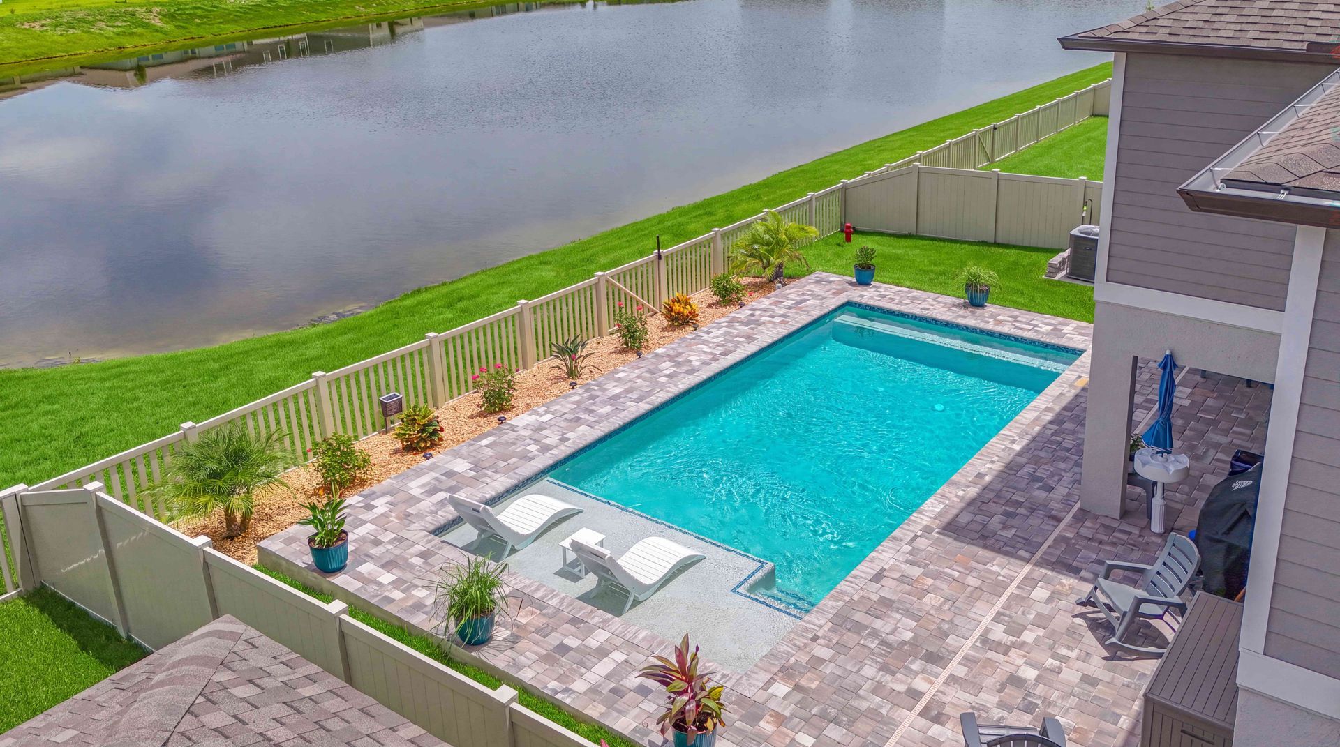 Backyard pool with patio, lounge chairs, and a fenced yard beside a pond