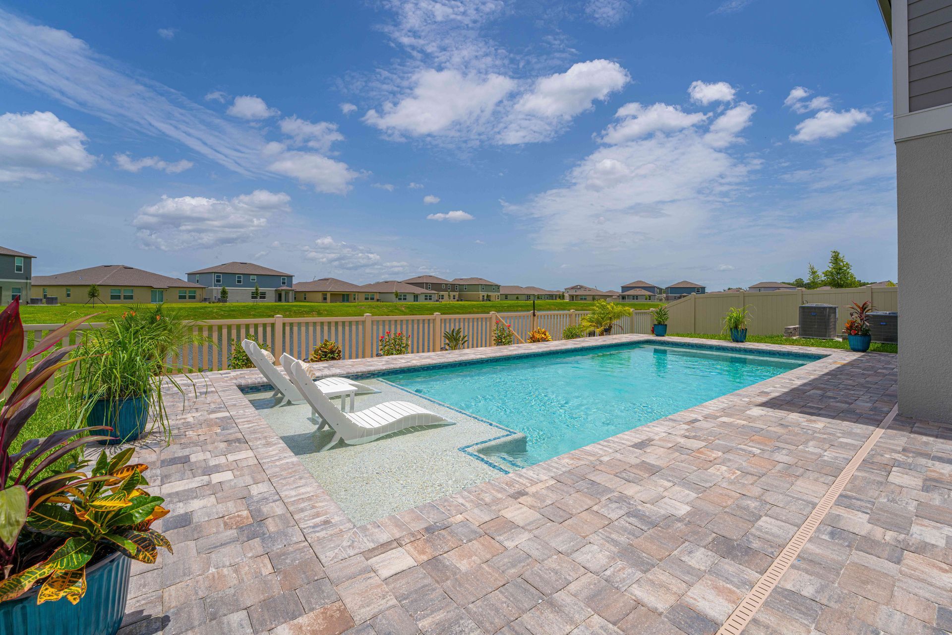Outdoor backyard pool with lounge chairs, stone deck, and open sky