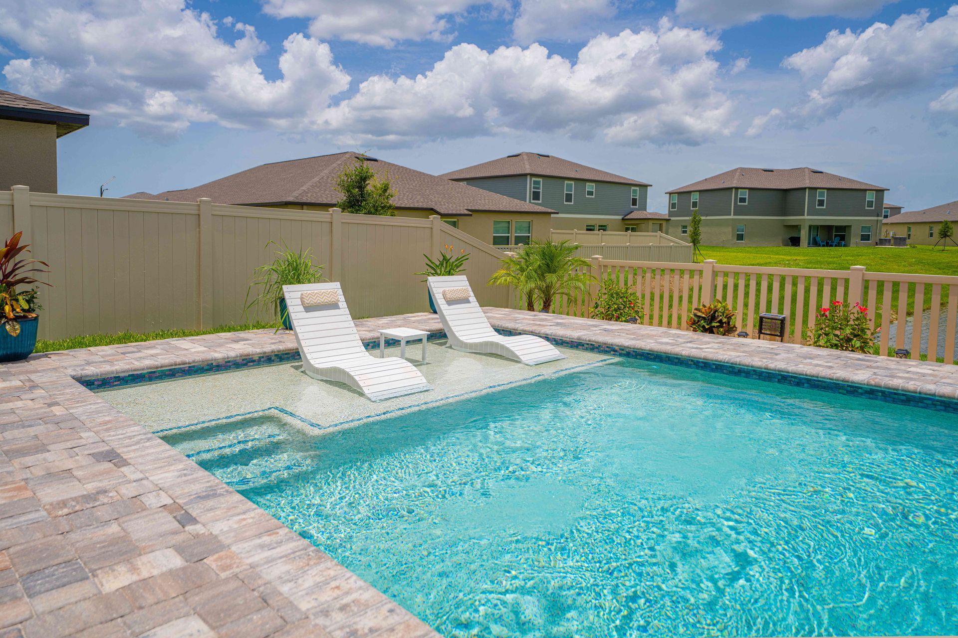 Backyard swimming pool with two white lounge chairs and a fenced suburban view under a partly cloudy sky
