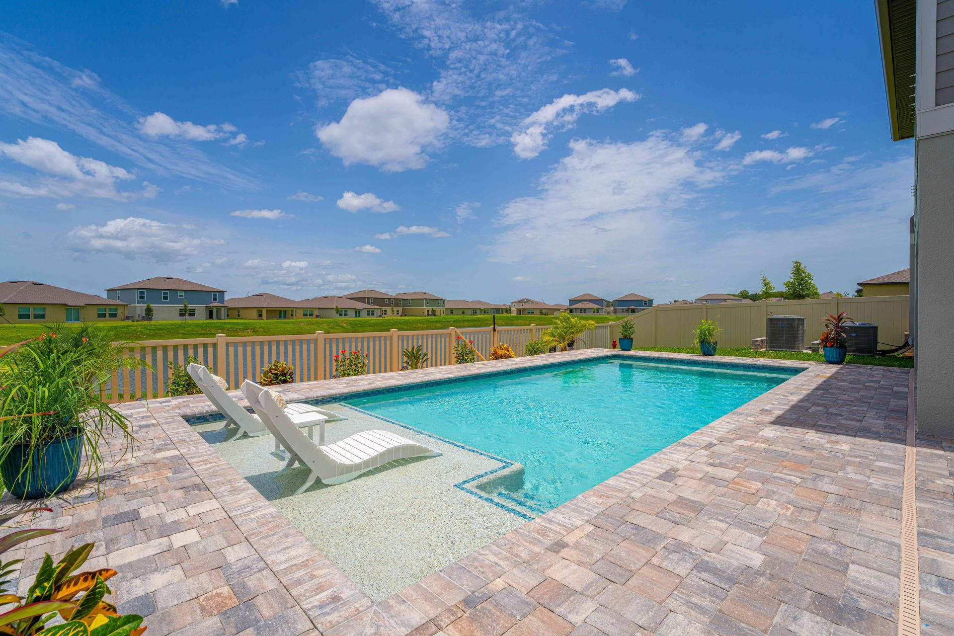 Backyard swimming pool with lounge chairs, brick patio, and a clear blue sky